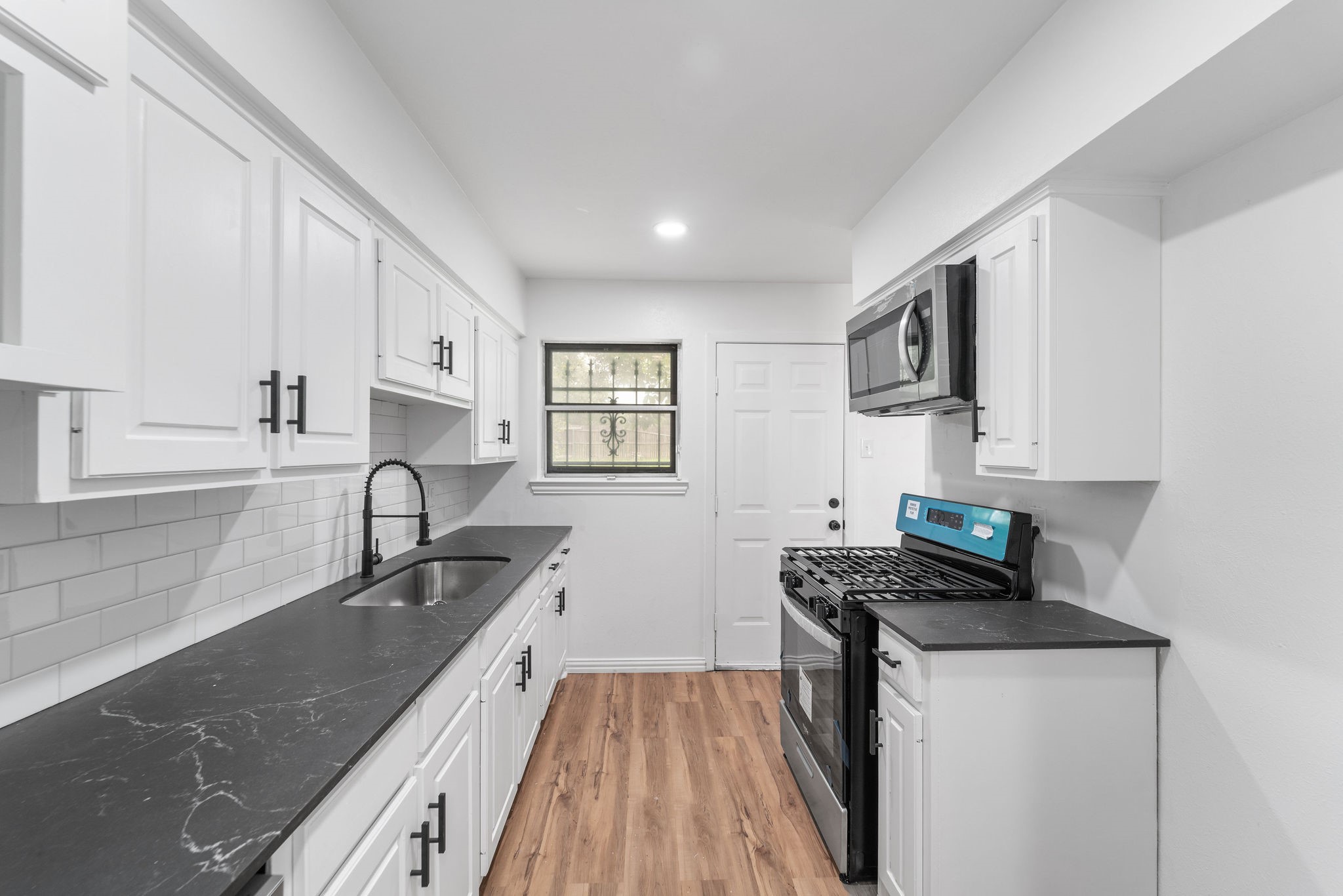 Kitchen with white cabinets, dark countertops, subway tile backsplash, stainless appliances, and wood-look floors.