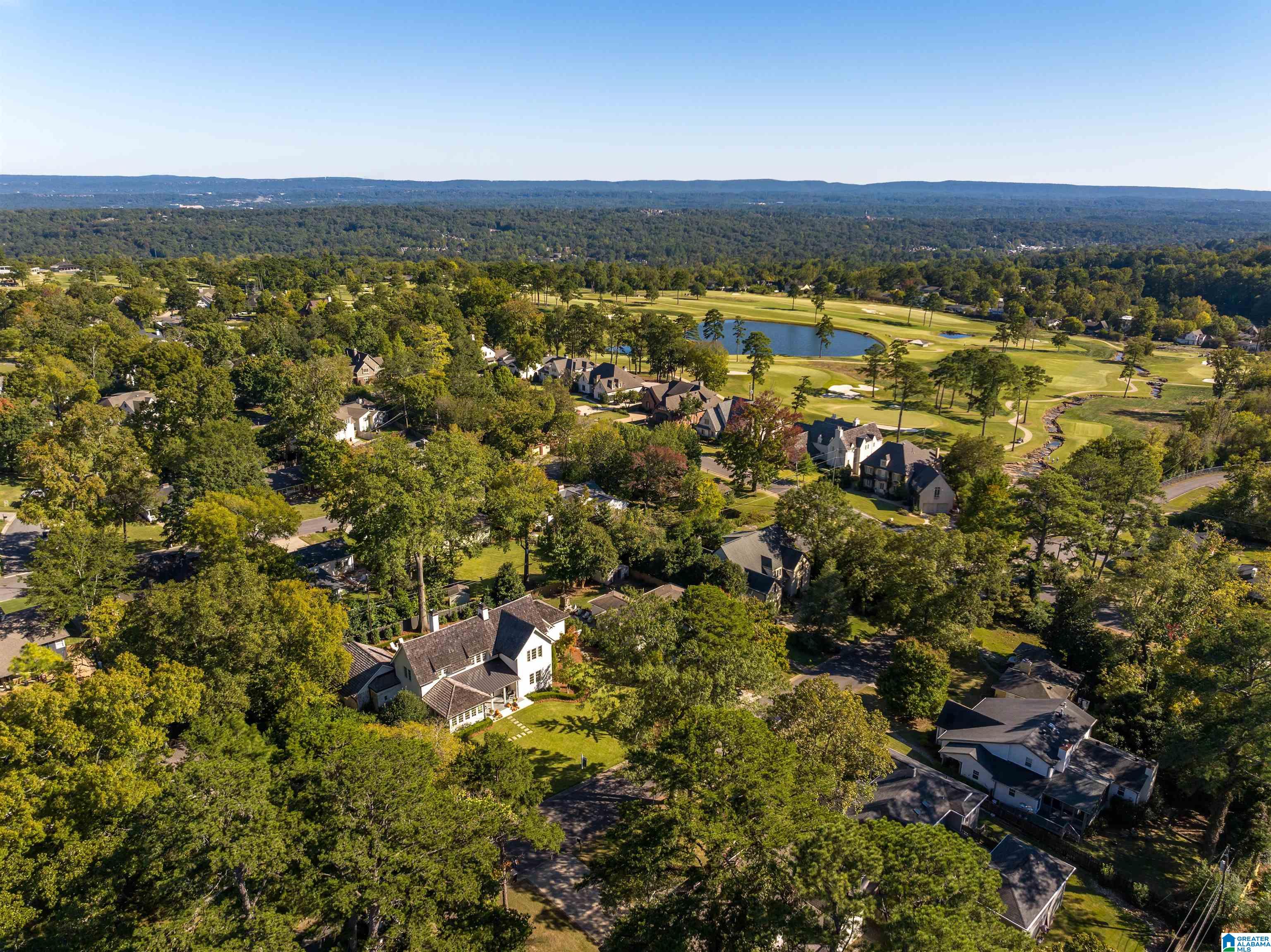 Aerial view of a leafy neighborhood beside a golf course and pond.
