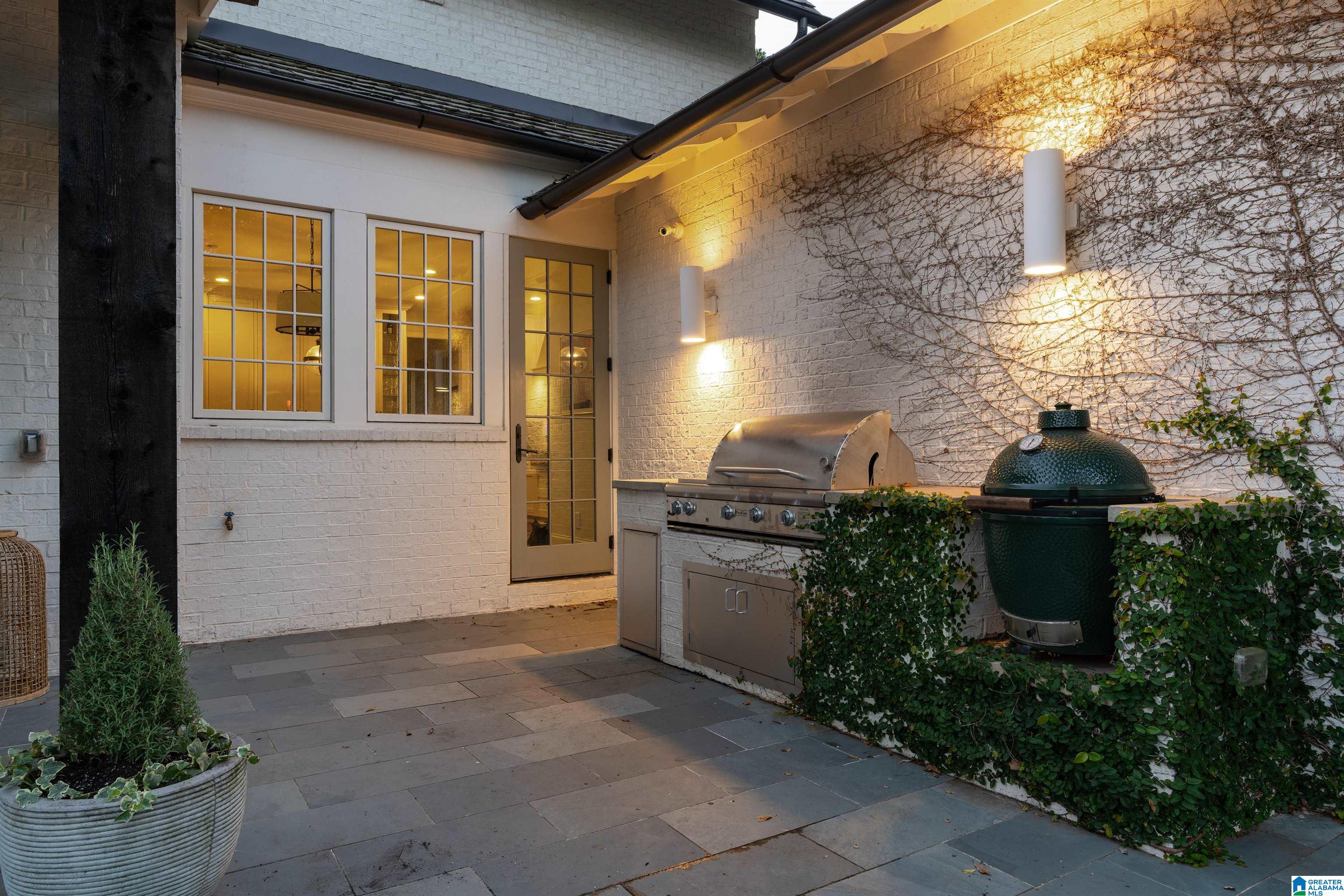 Outdoor patio kitchen with two grills beside white brick walls and vine-covered masonry.