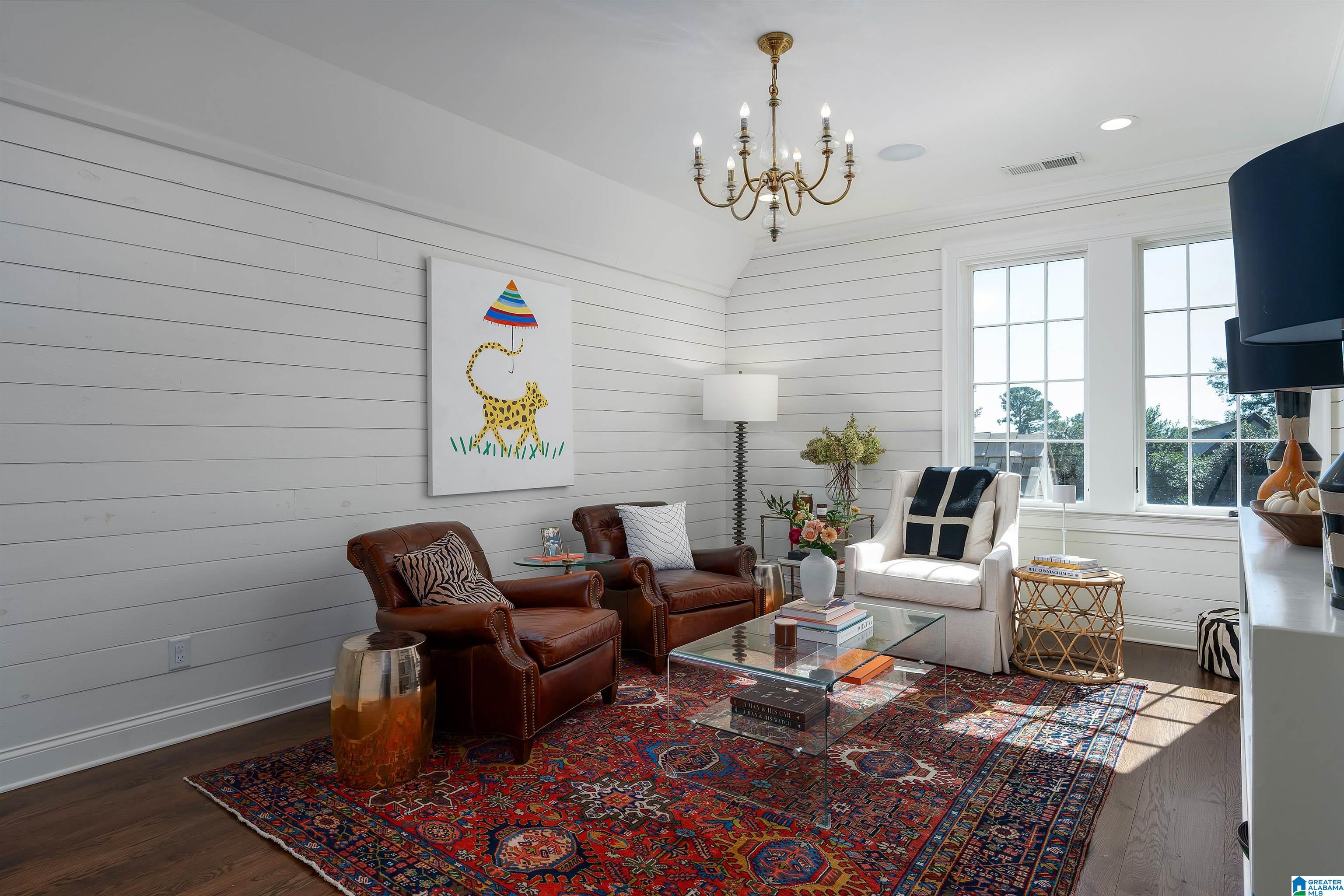 Staged living room with leather armchairs, a colorful patterned rug, and tall sunlit windows.