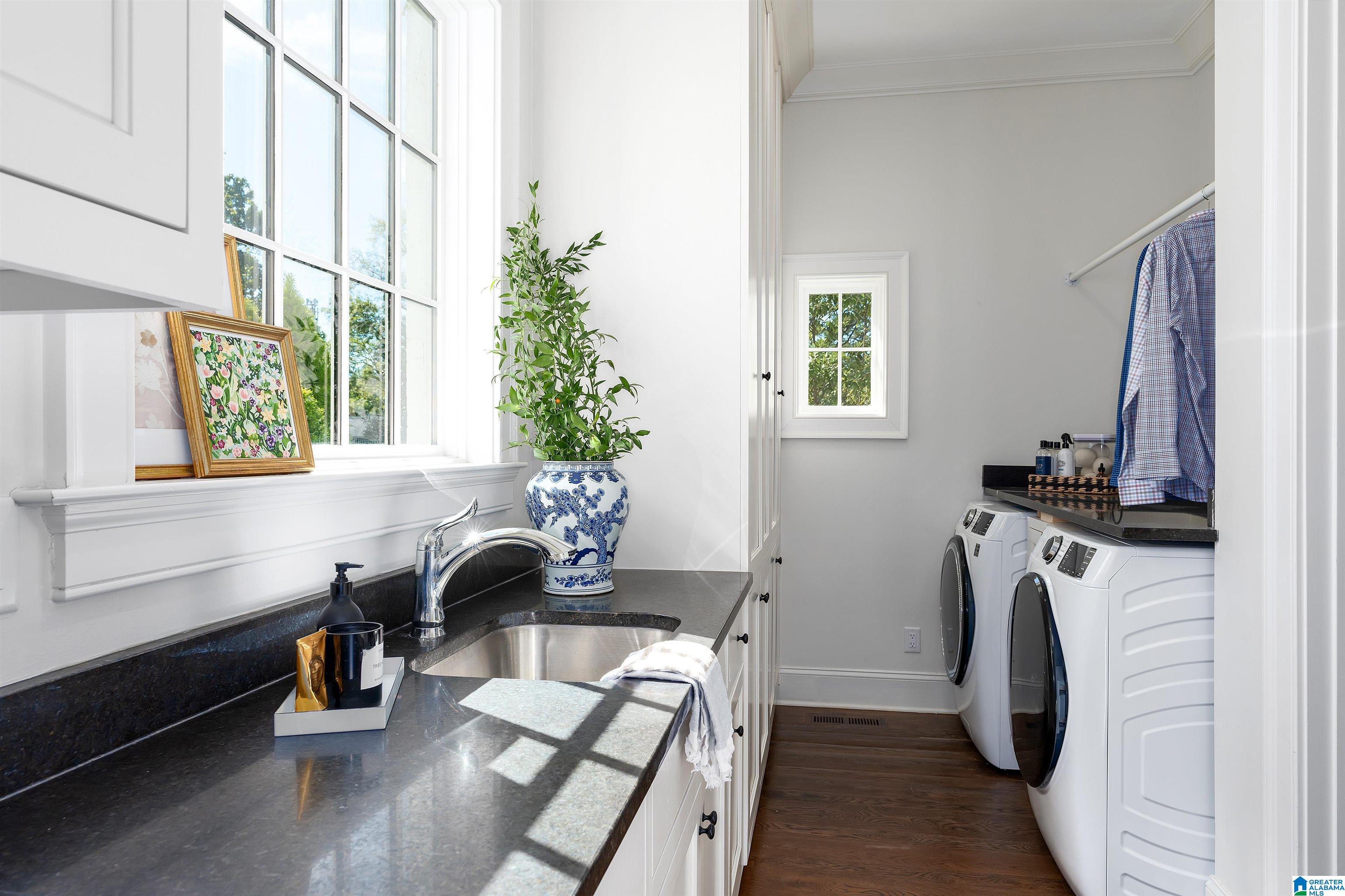 Laundry room with a window-side sink and dark countertop beside a washer and dryer.