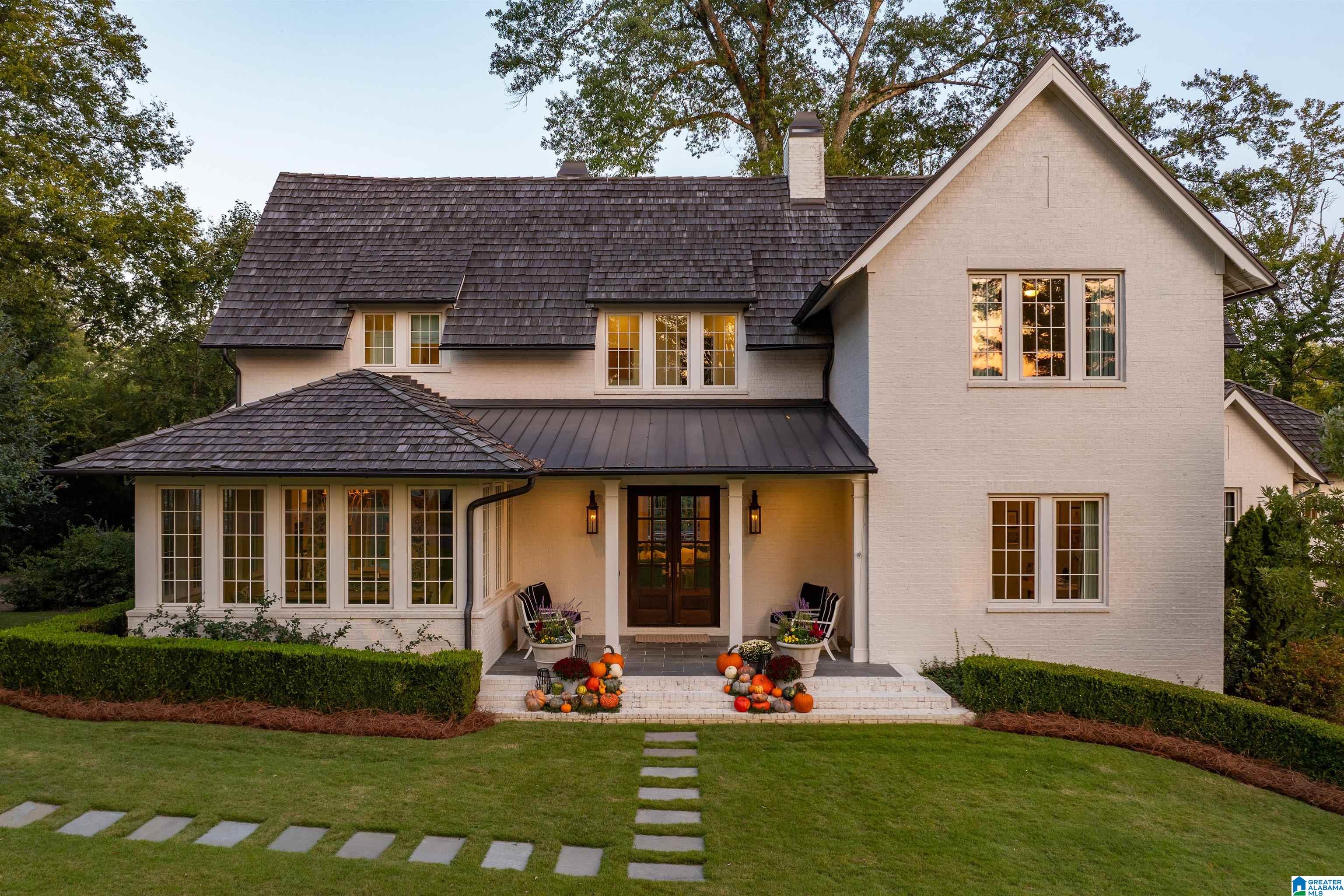 Two-story white brick home with a dark shingle roof and pumpkins decorating the front steps.