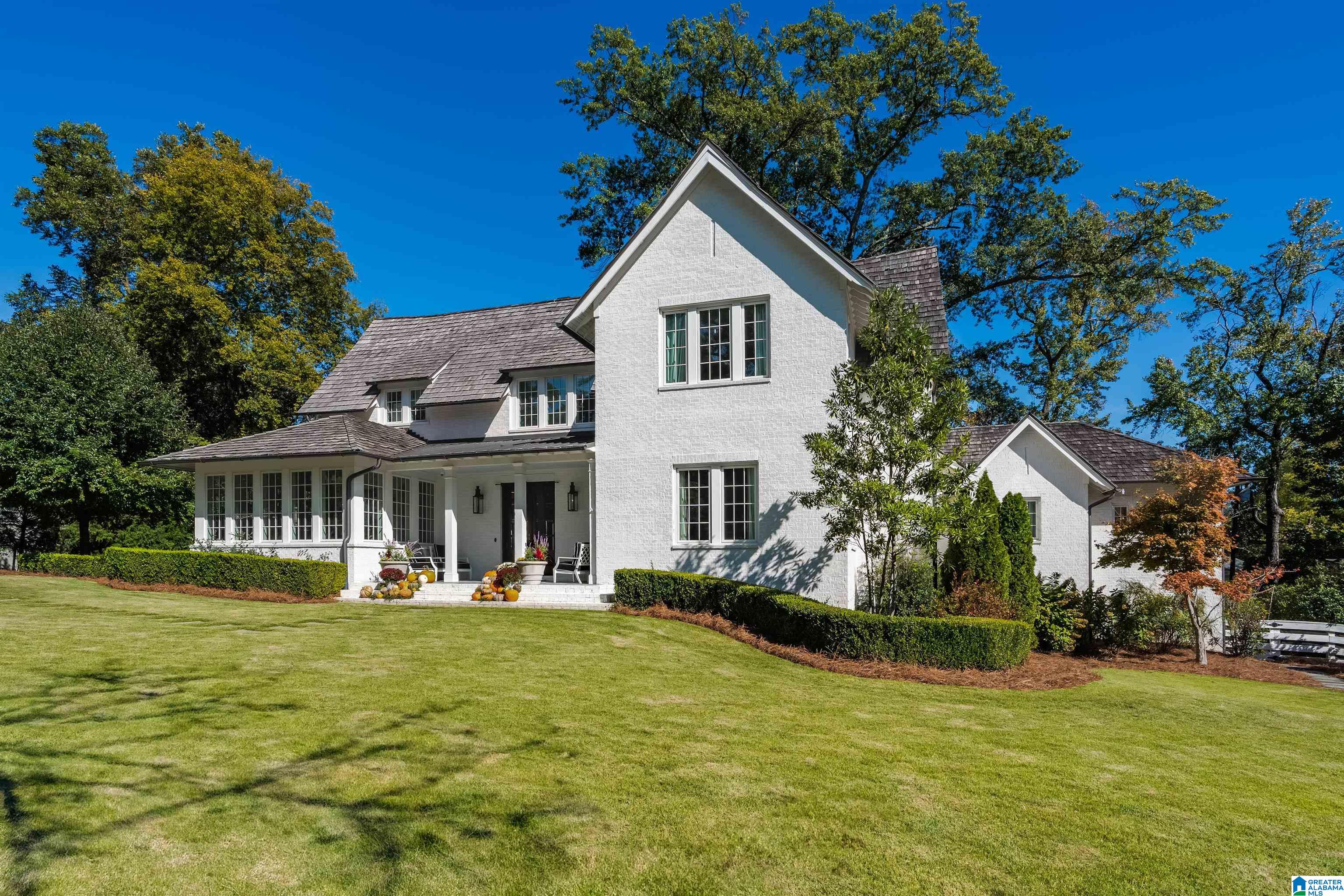 White brick two-story home with steep gables, a covered entry, and a broad landscaped lawn.