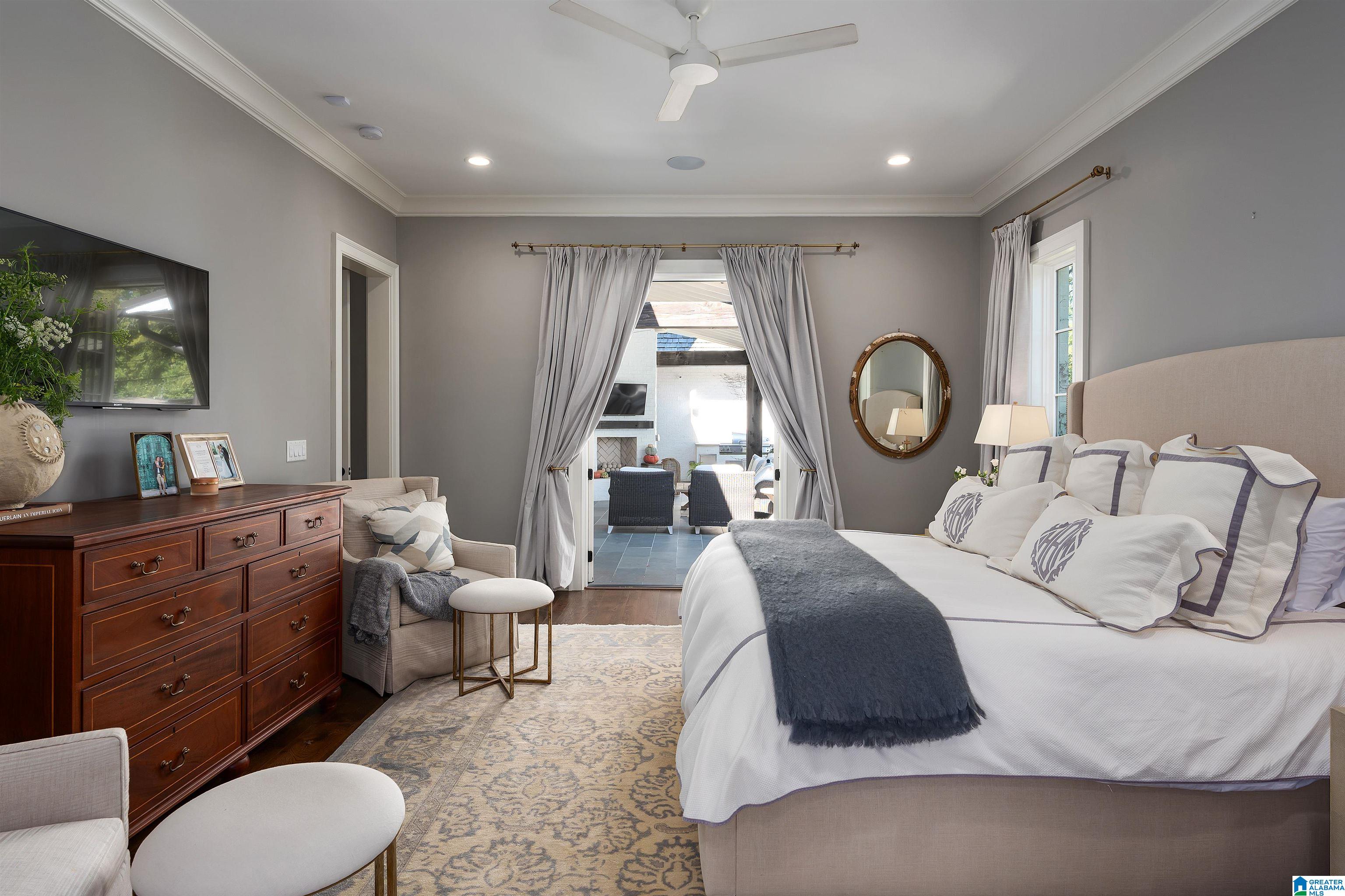 Furnished bedroom with an upholstered bed and dark wood dresser, opening onto a tiled patio.