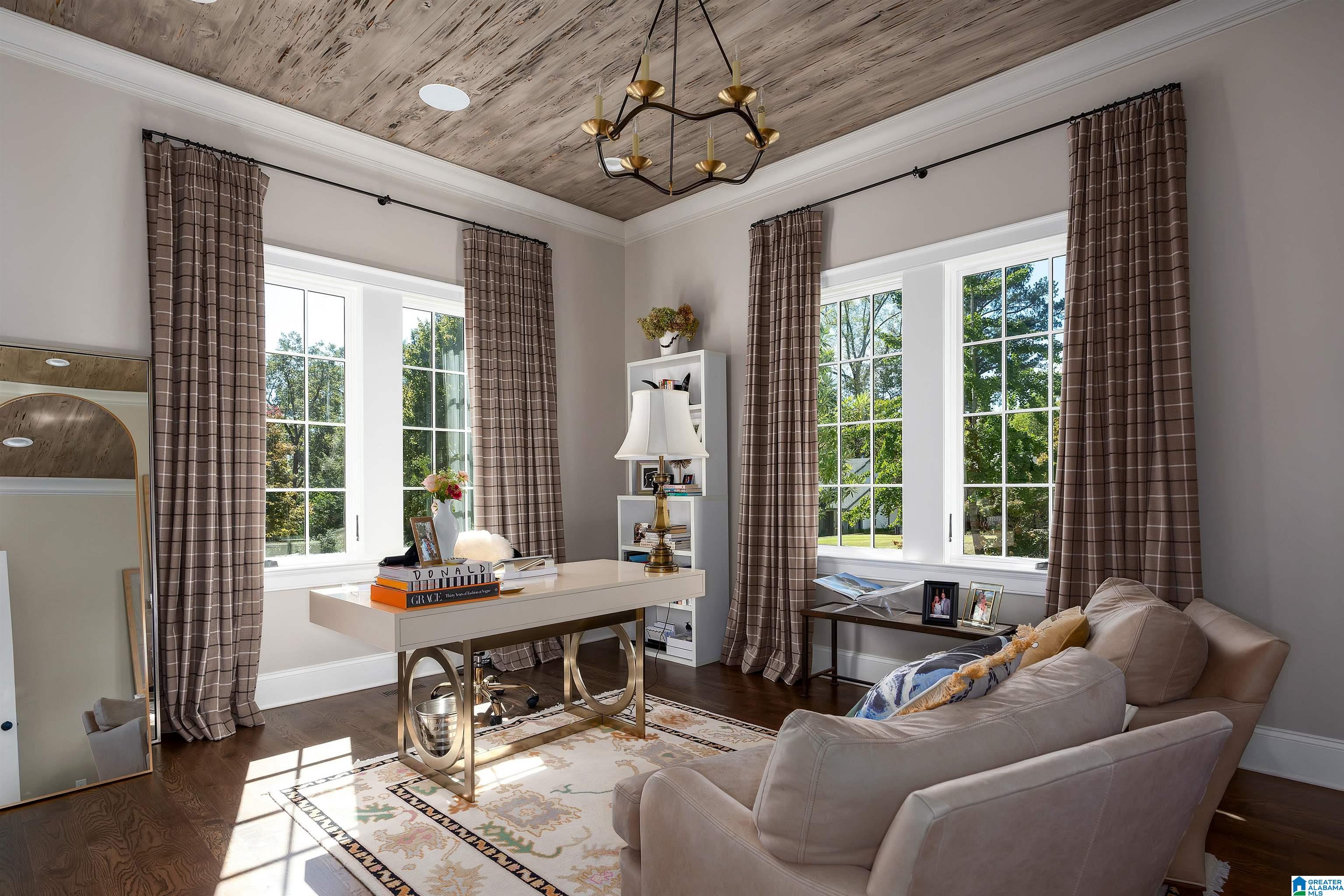 Home office with a desk, pale sofa, tall curtained windows, and a weathered wood ceiling.