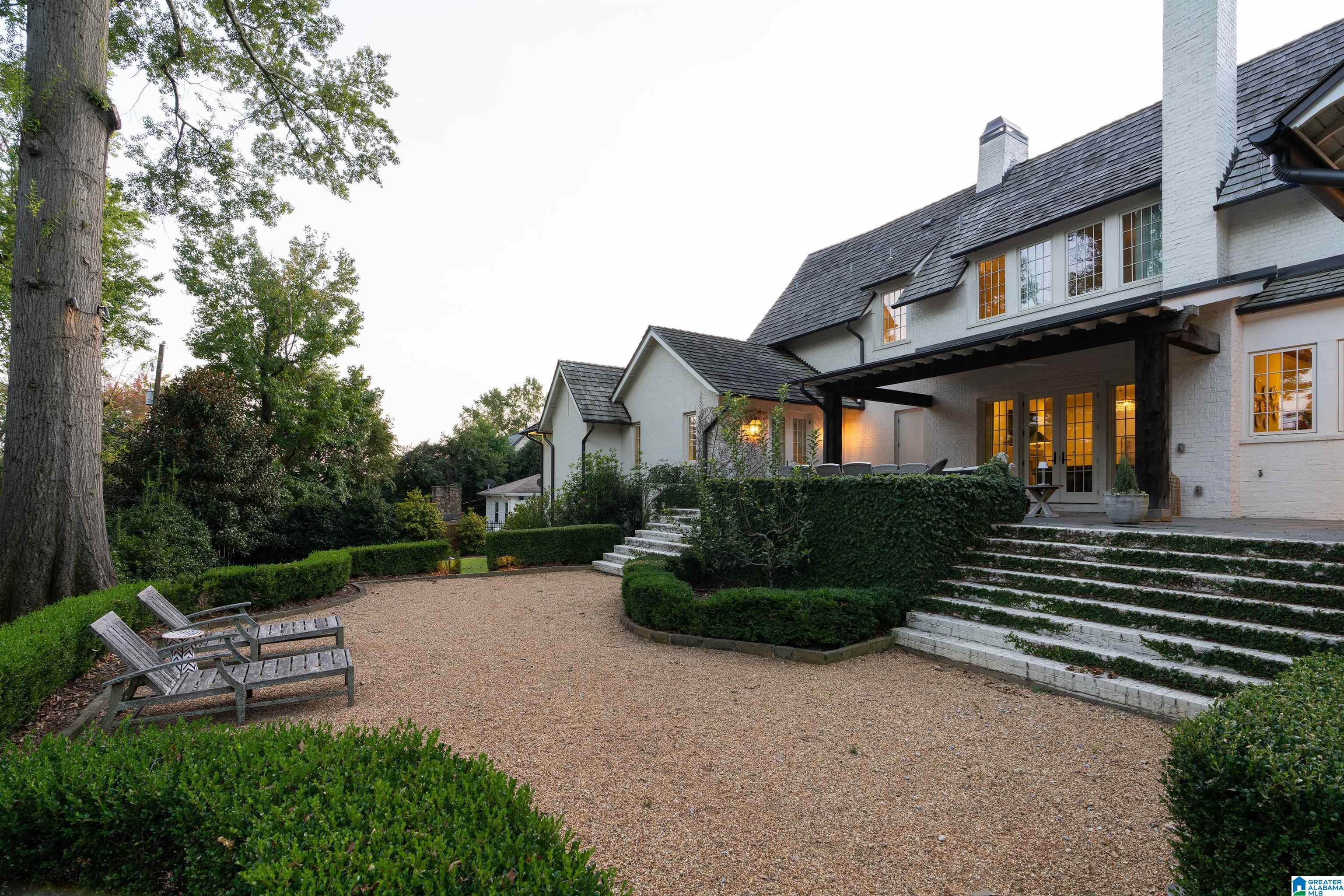 White brick home with a covered patio and stone steps overlooking a gravel courtyard.