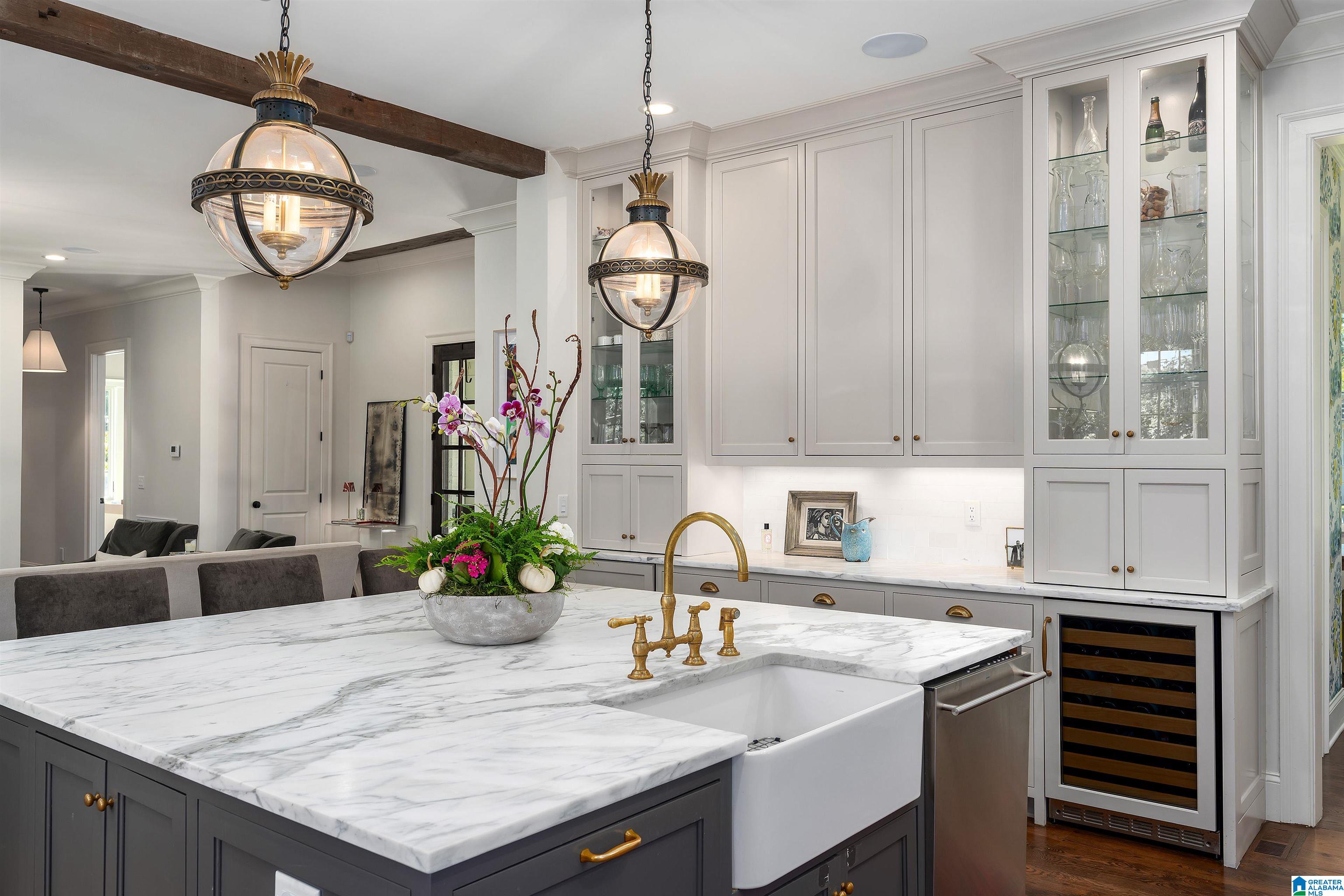 Kitchen with a marble island, farmhouse sink, brass fixtures, and glass-front cabinets.