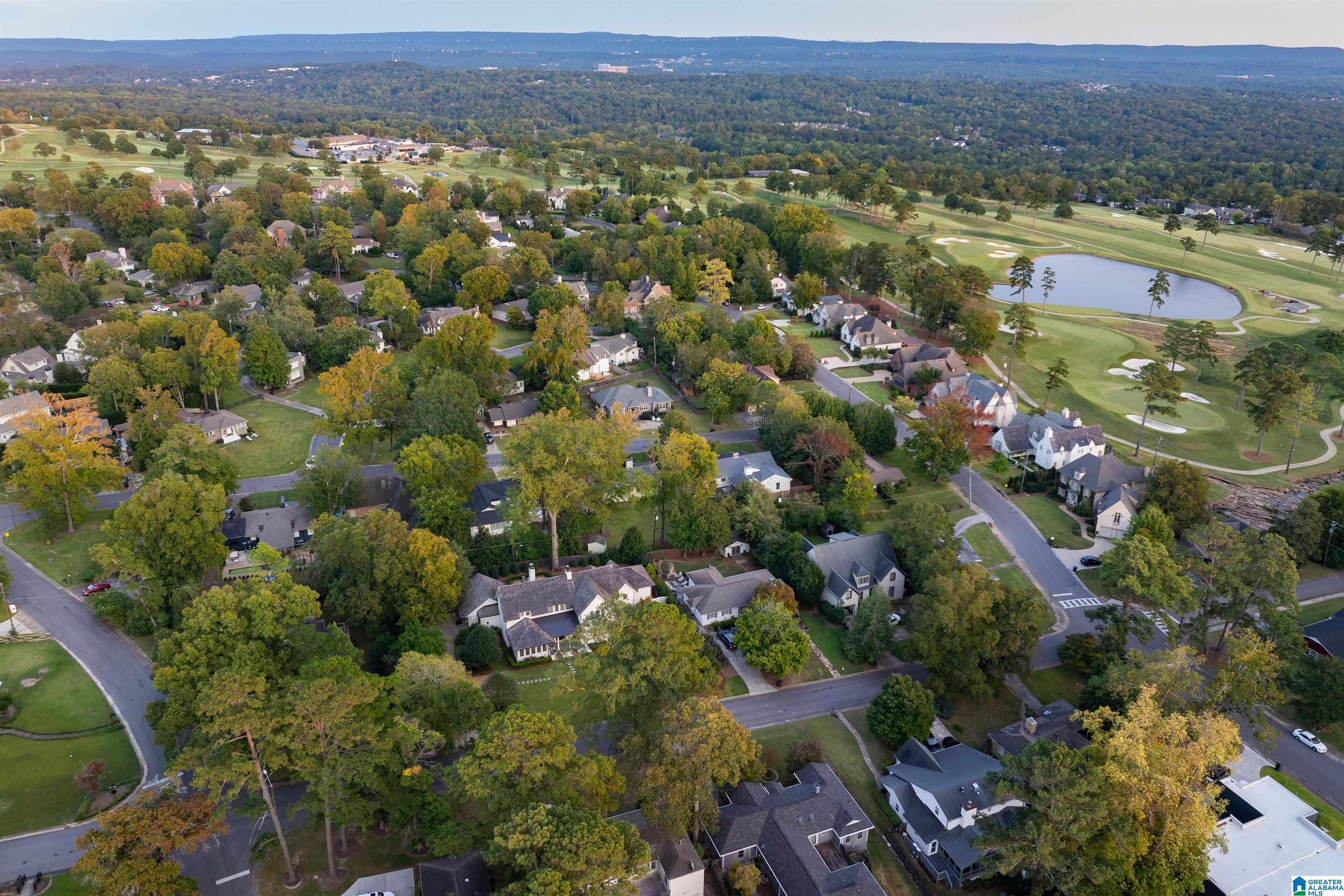 Aerial view of a tree-lined neighborhood beside a golf course and pond.