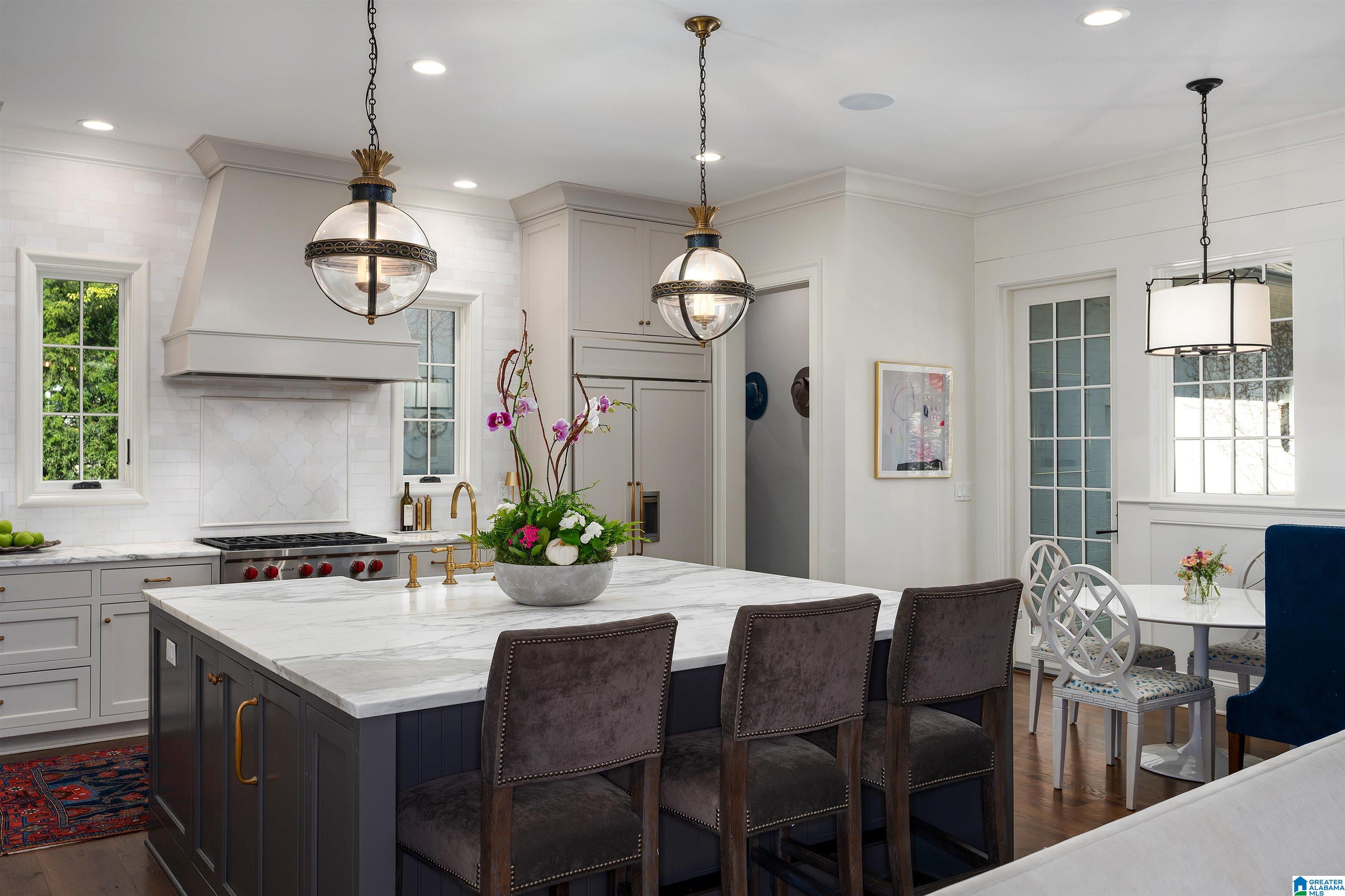 Bright kitchen with a marble-topped island, dark bar stools, brass pendants, and adjoining dining area.