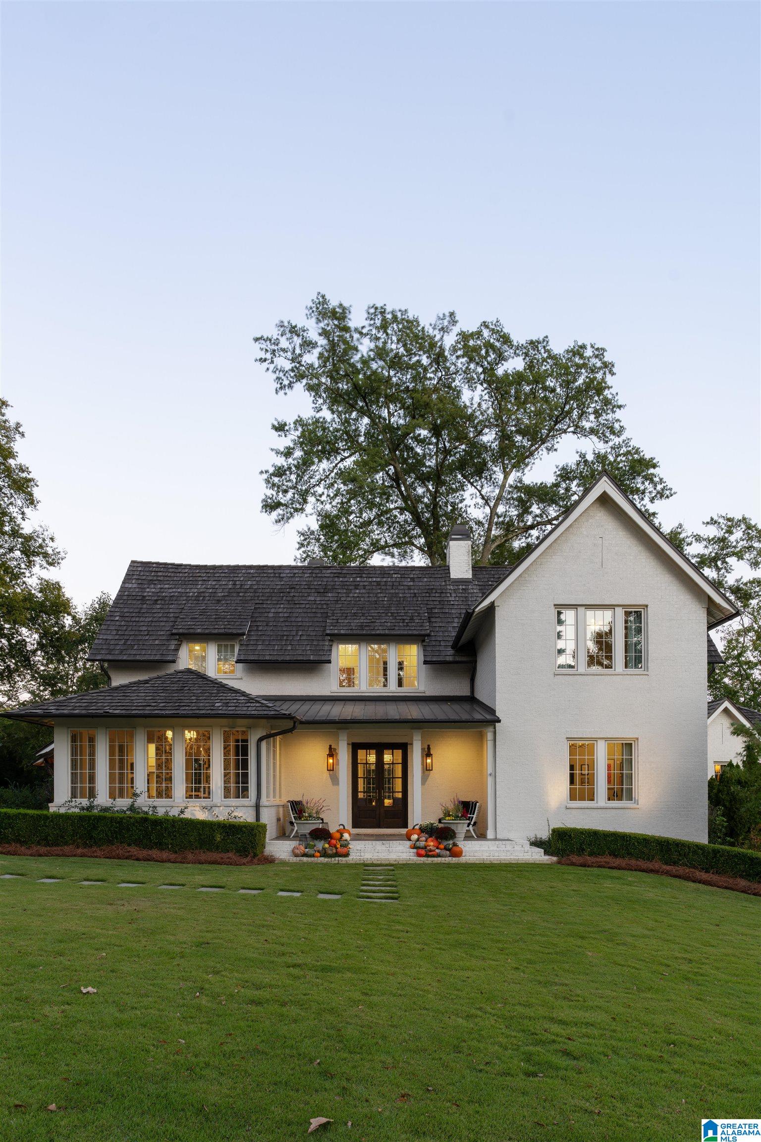 White two-story house with dark shingle roof, pumpkin-decorated entry, and broad green lawn.
