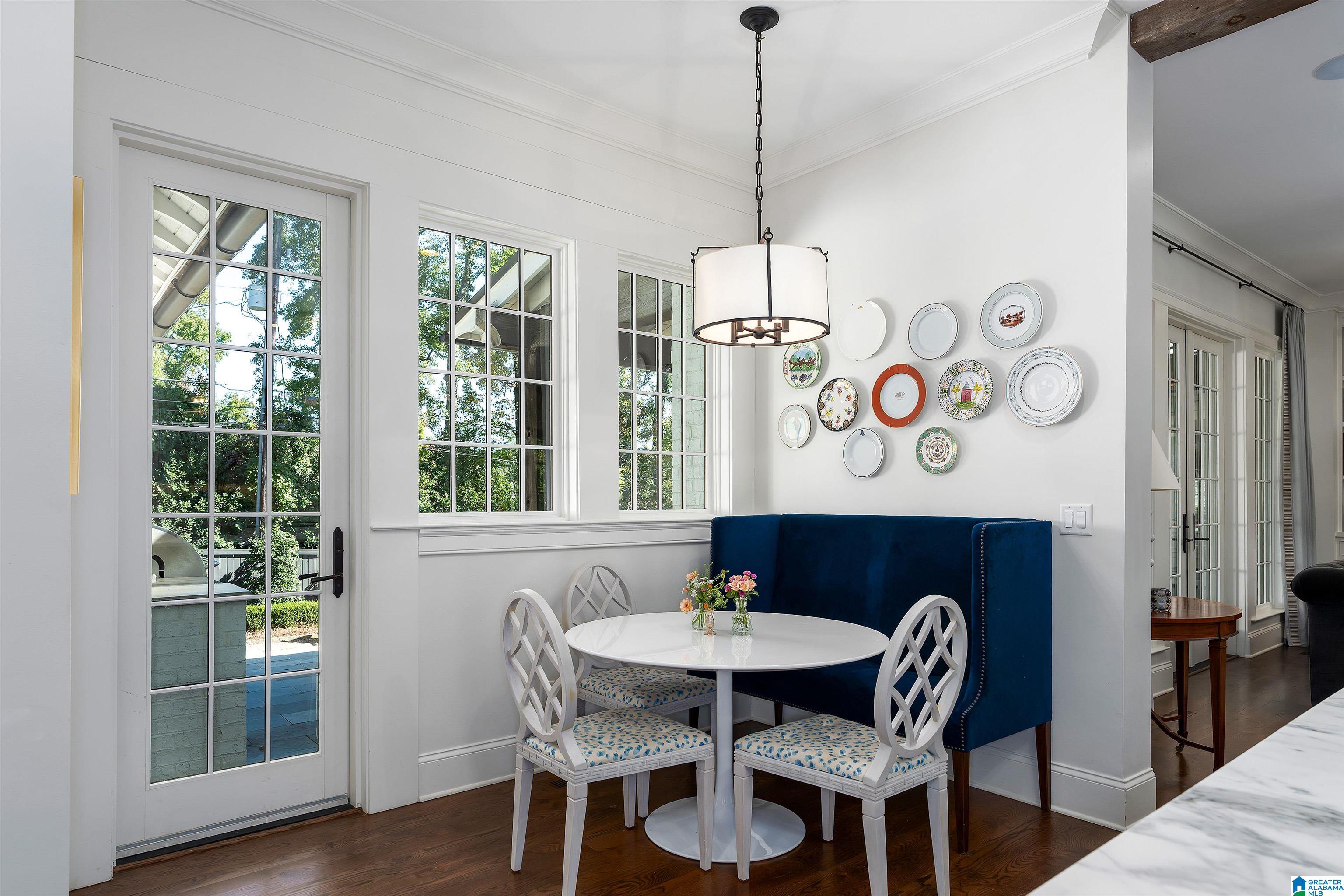 Dining nook with a round white table, blue banquette, decorative plates, and tall glass doors.