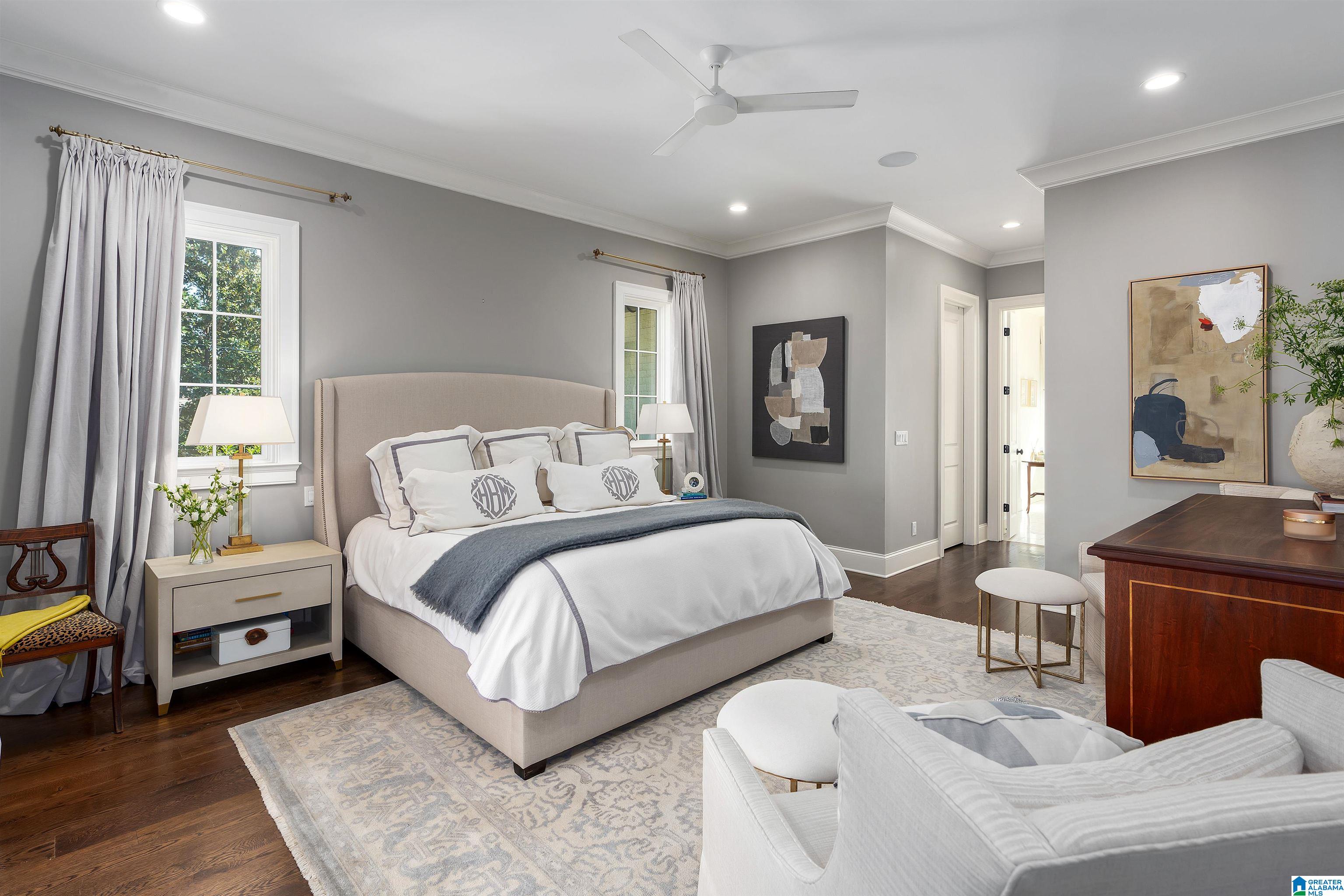 Staged bedroom with a king bed, gray walls, patterned rug, and sitting area.