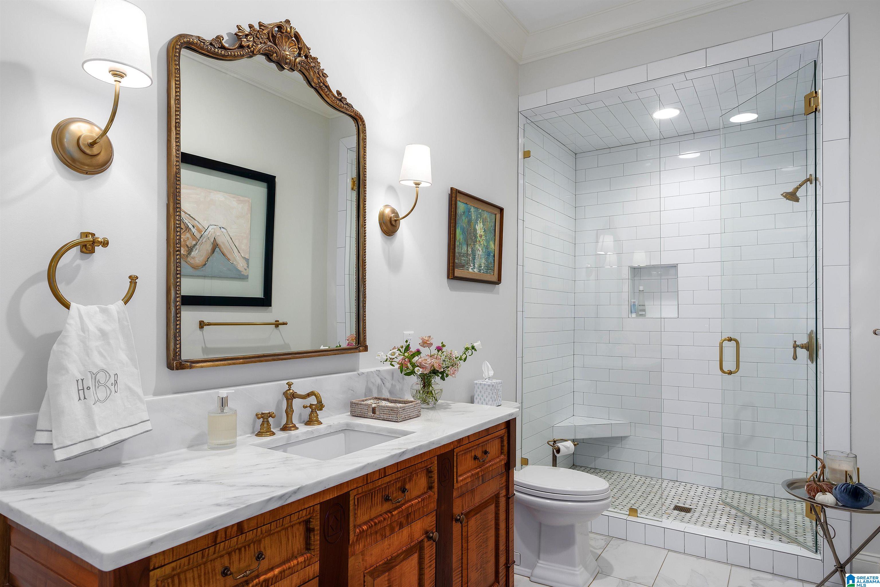 Bathroom with a carved wood vanity, marble countertop, ornate mirror, and glass-enclosed tiled shower.