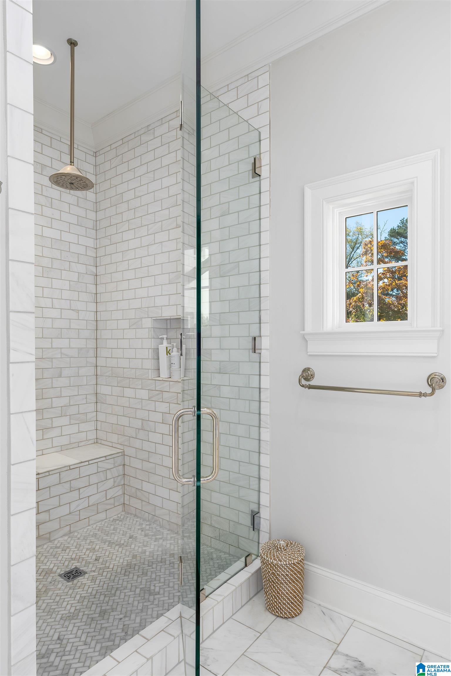 Walk-in shower with white tile, a built-in bench, and glass enclosure beside a window.