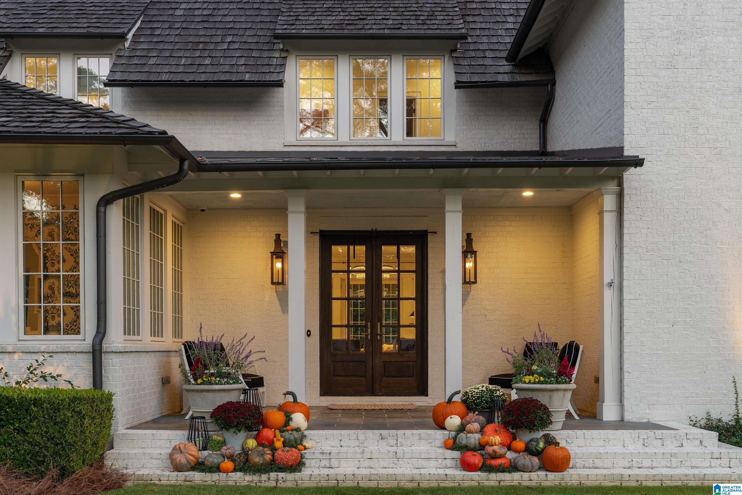 White brick home entrance with a covered porch, dark double doors, and autumn pumpkins on the steps.