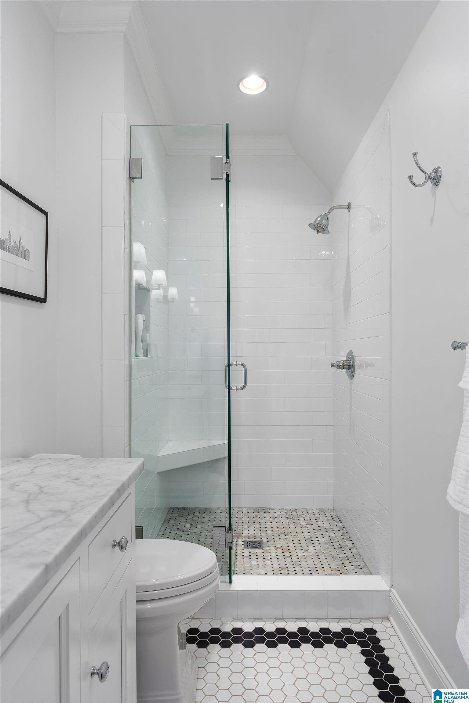 Bathroom with a glass-enclosed white tile shower, marble vanity, and black-and-white hexagonal floor.