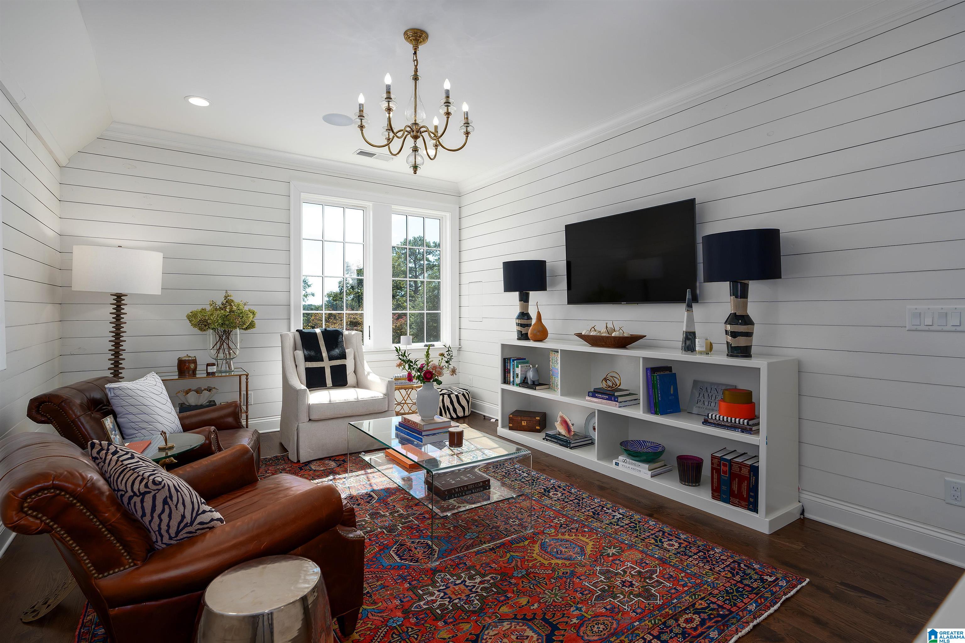 Living room with a brown leather sofa, white armchair, large patterned rug, and television.