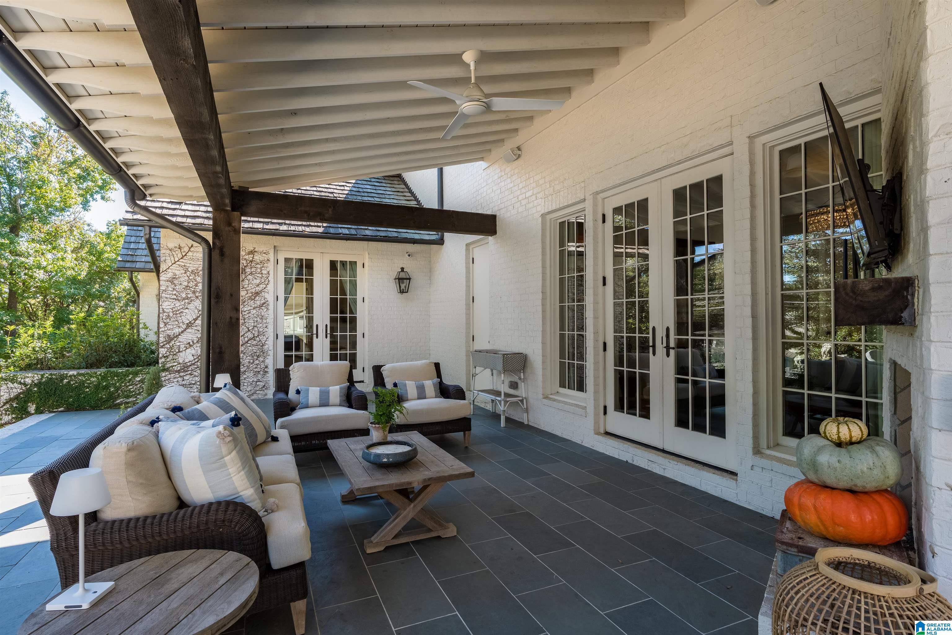 Covered outdoor patio with wicker seating, dark tile flooring, French doors, and autumn pumpkins.