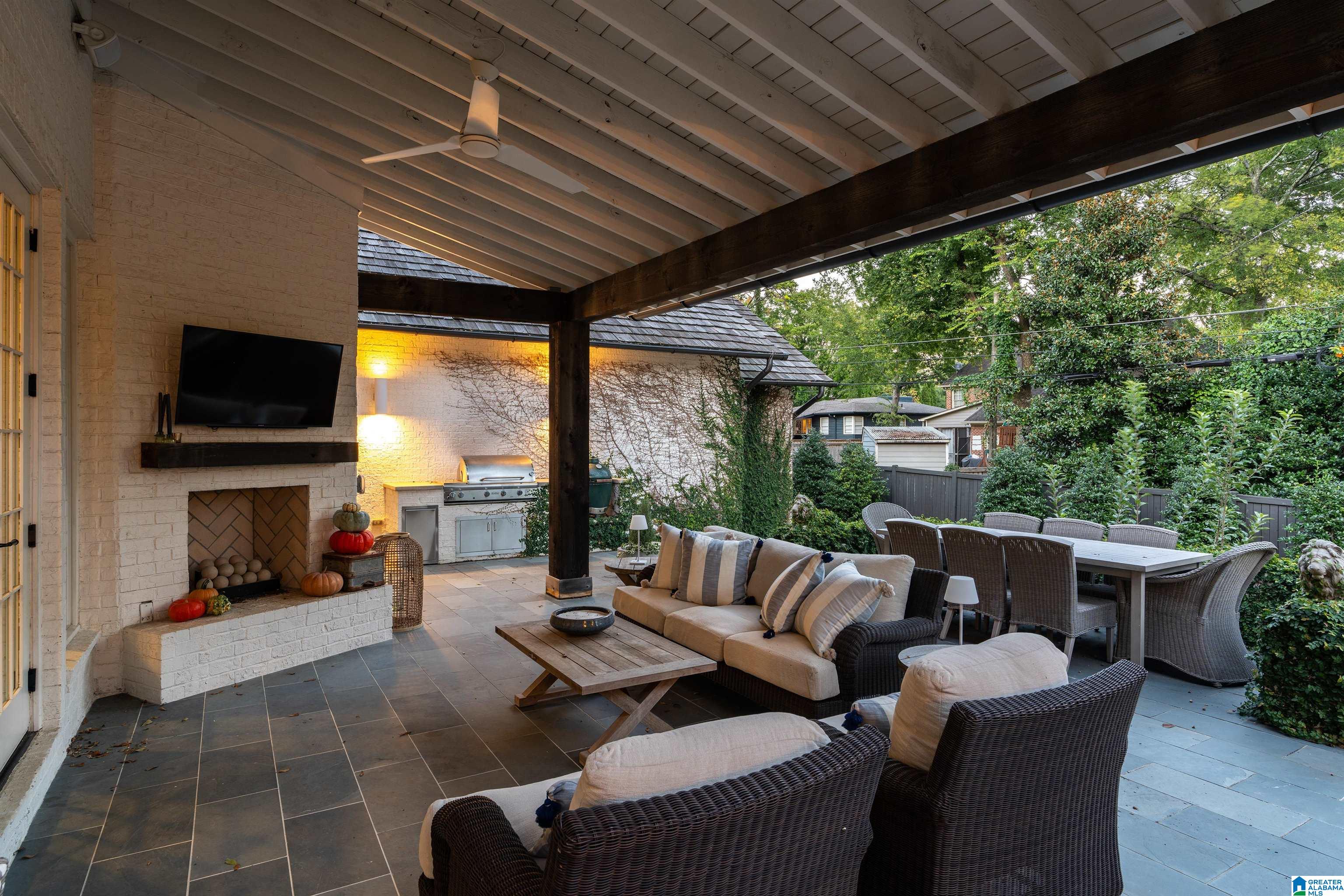Covered patio with a brick fireplace, outdoor grill, wicker seating, and dining area.