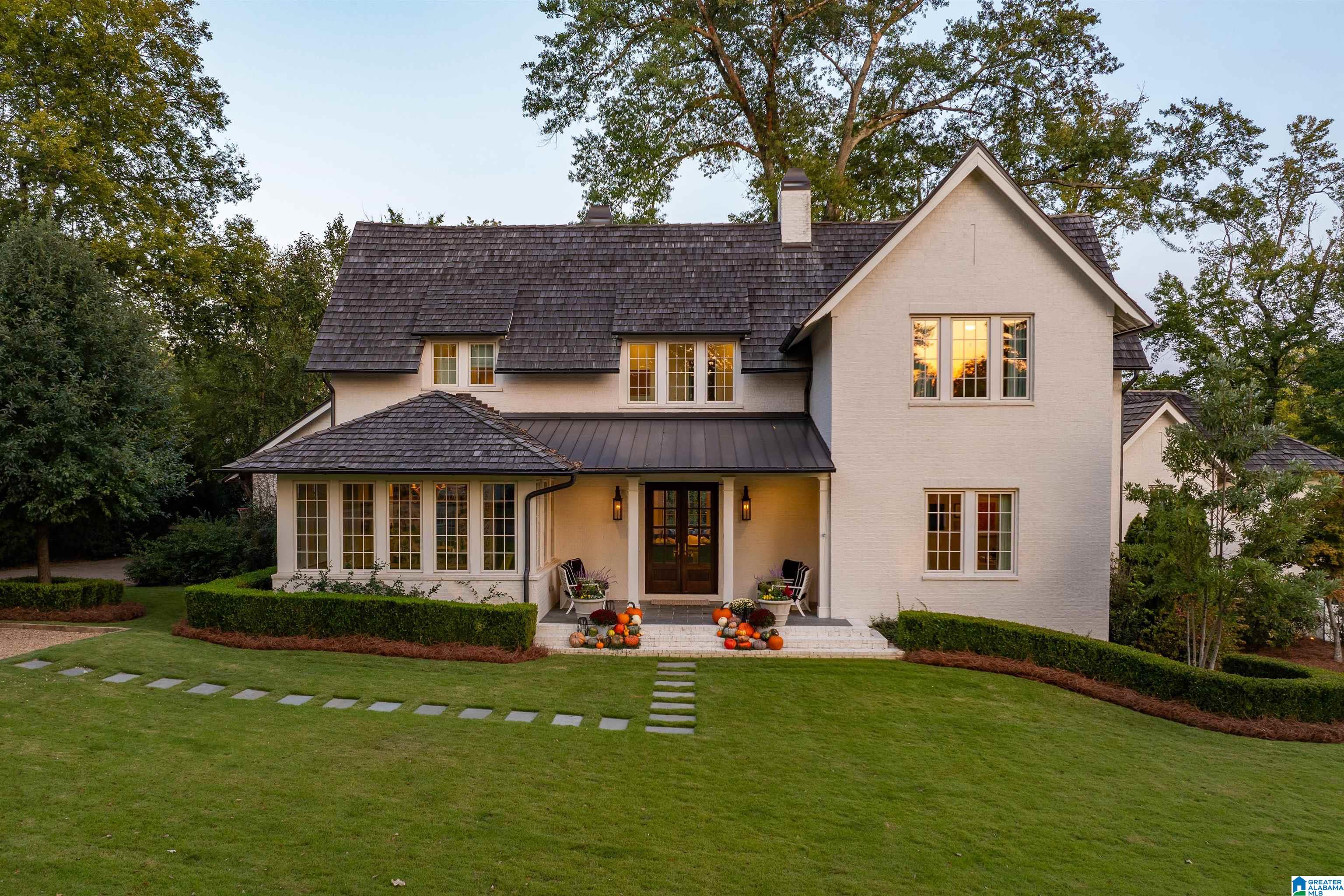 White brick two-story home with a dark roof, broad lawn, and pumpkin-decorated front steps.
