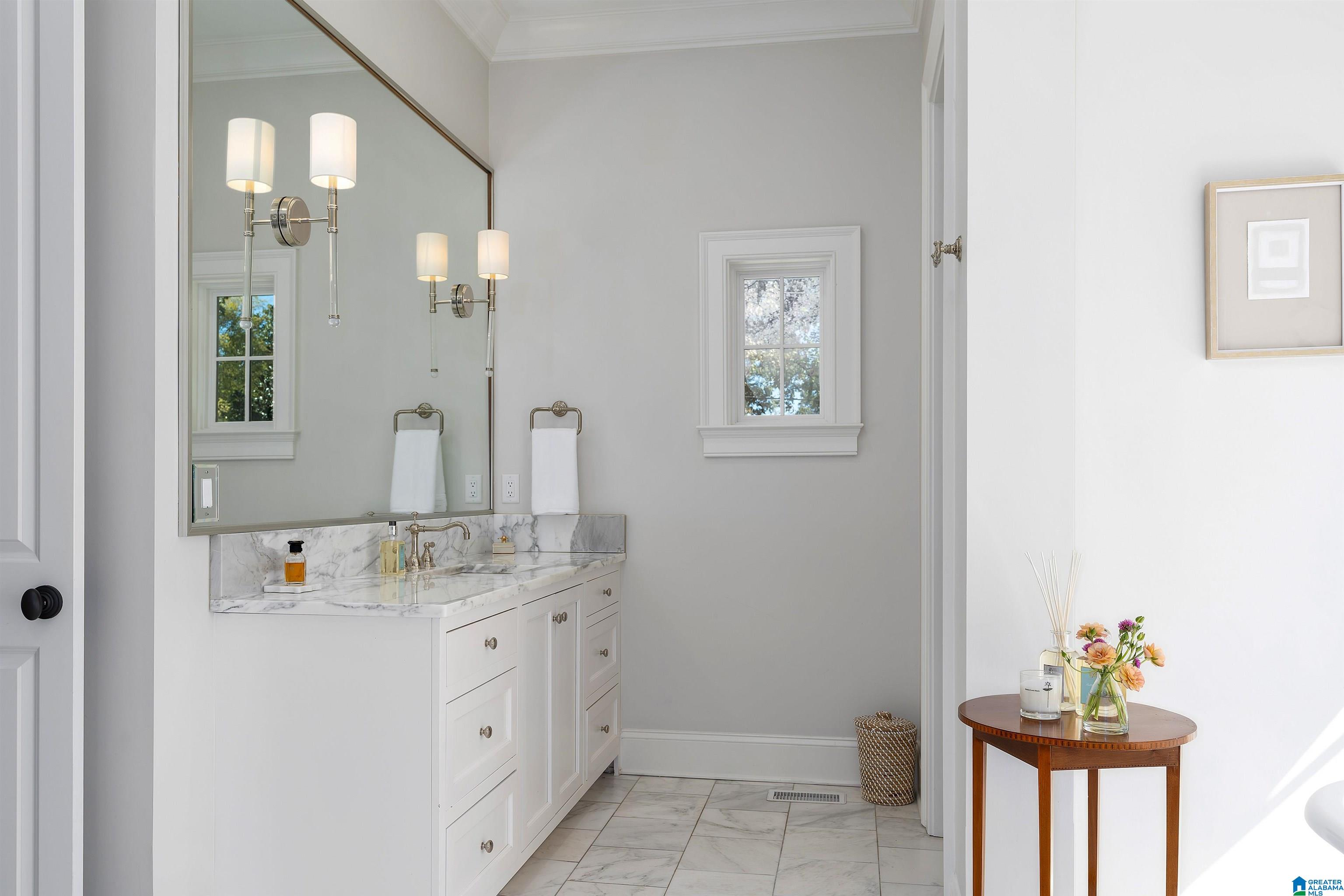 Bright bathroom with a white vanity, veined marble counters, a large mirror, and a small window.
