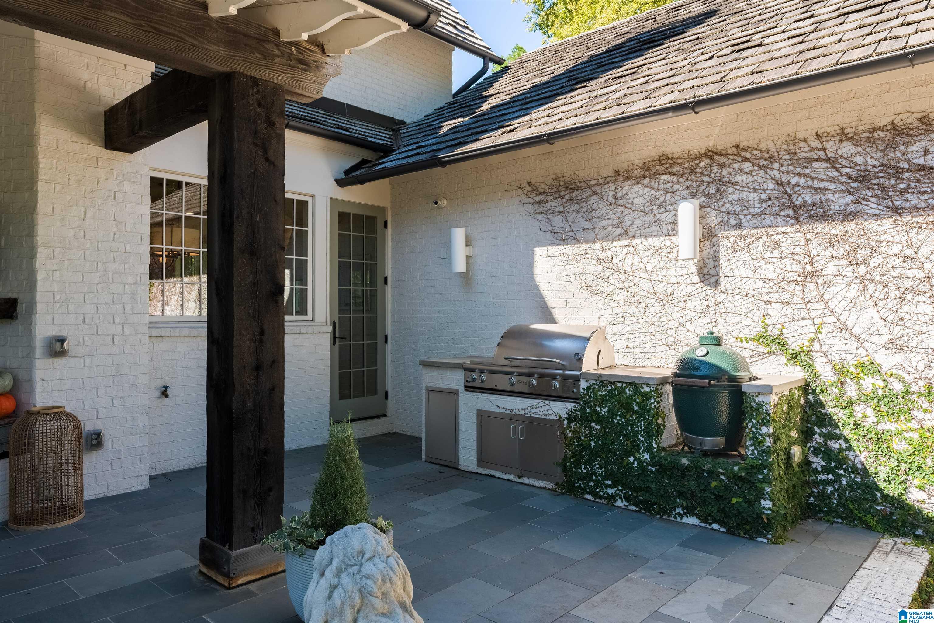 Covered brick patio with built-in gas grill, green ceramic grill, and dark stone paving.