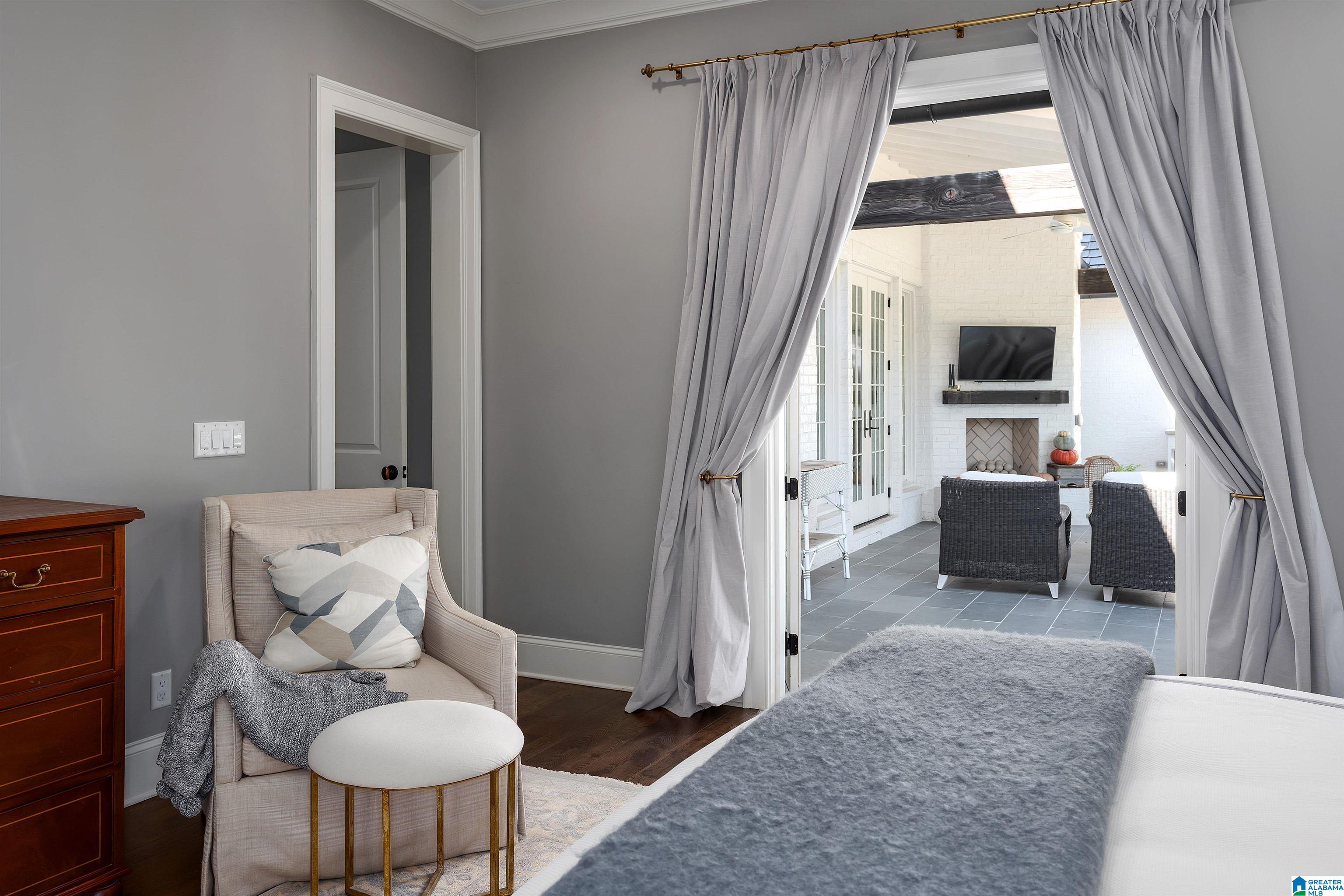 Bedroom with a beige armchair and open curtains overlooking a tiled patio with a fireplace.