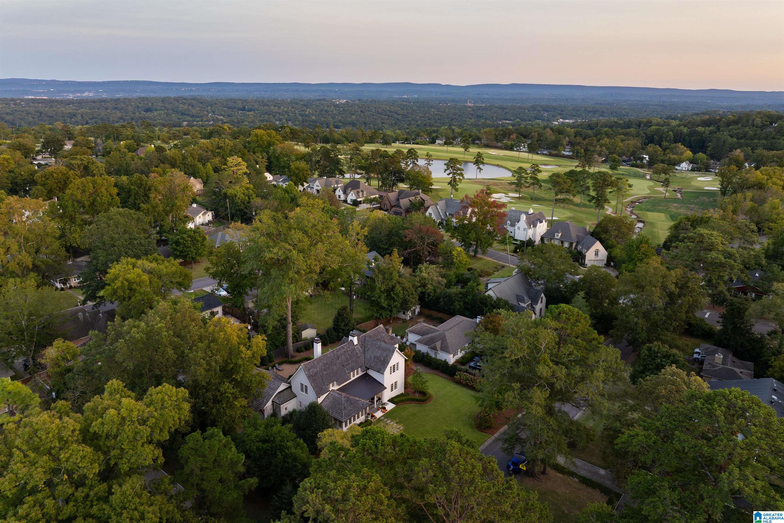Aerial view of a white home with a landscaped lawn, leafy neighborhood, and golf course beyond.