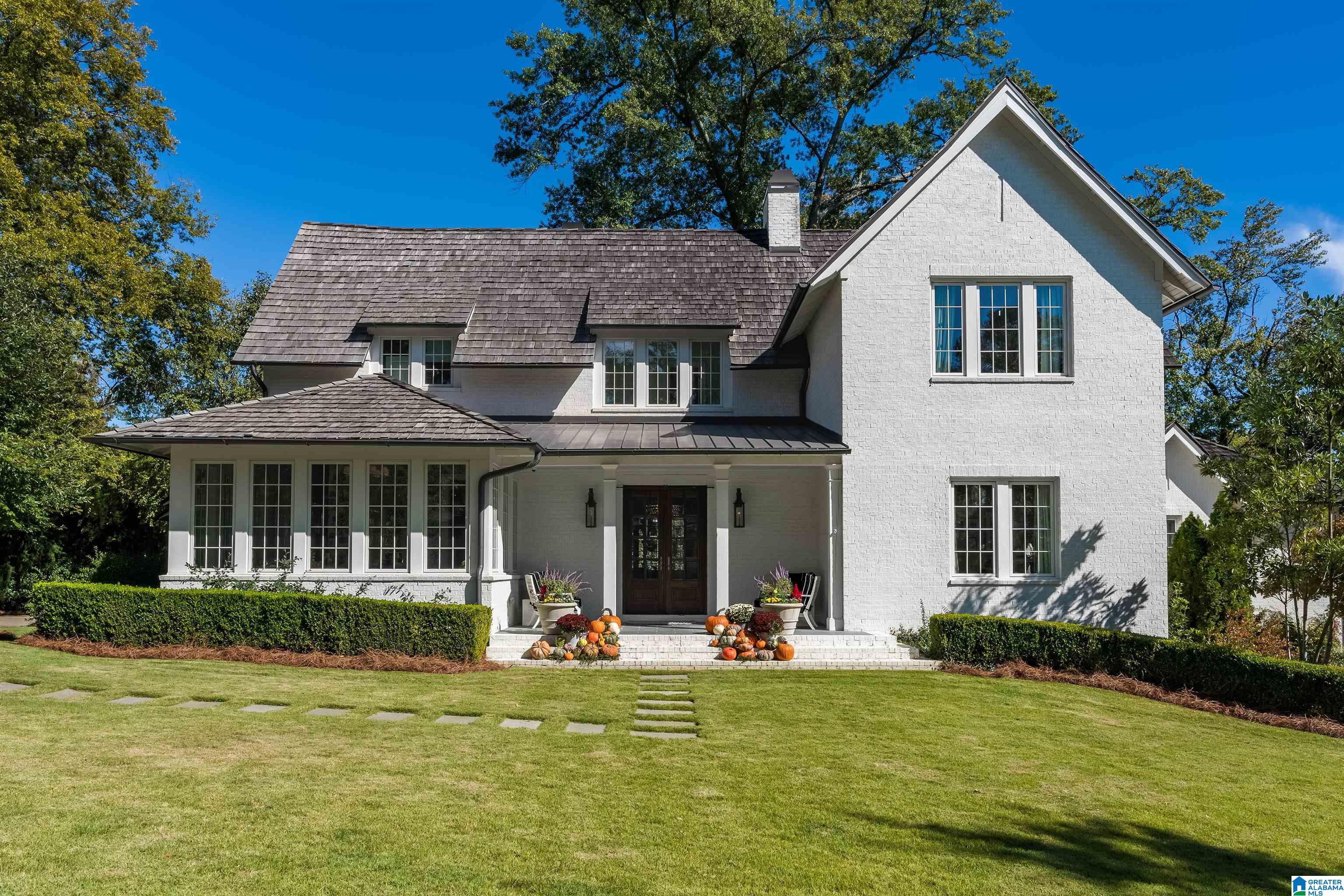 White brick two-story house with a steep shingle roof and pumpkin-decorated front steps.