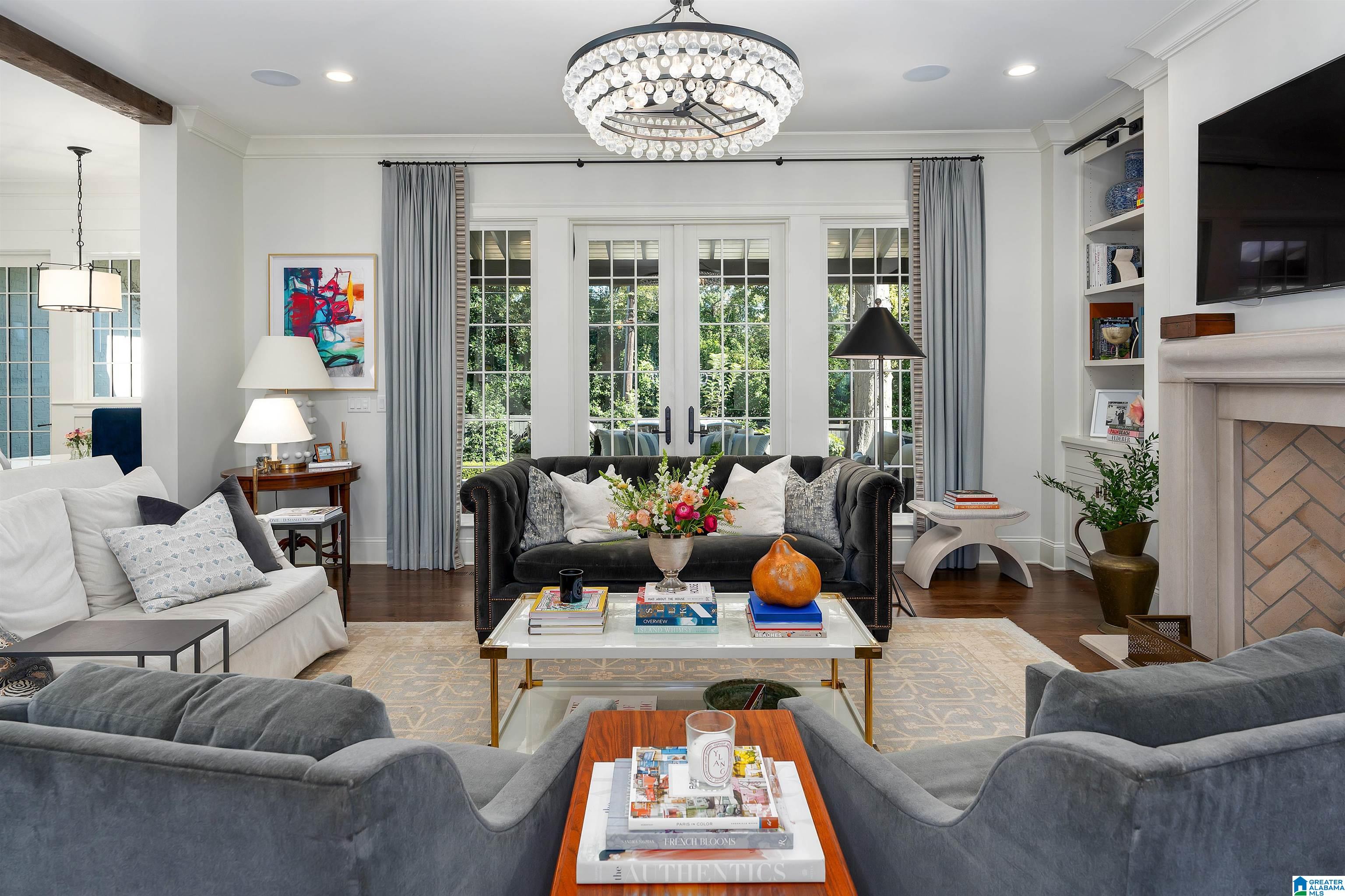 Furnished living room with a crystal chandelier, French doors, gray sofas, and a fireplace.
