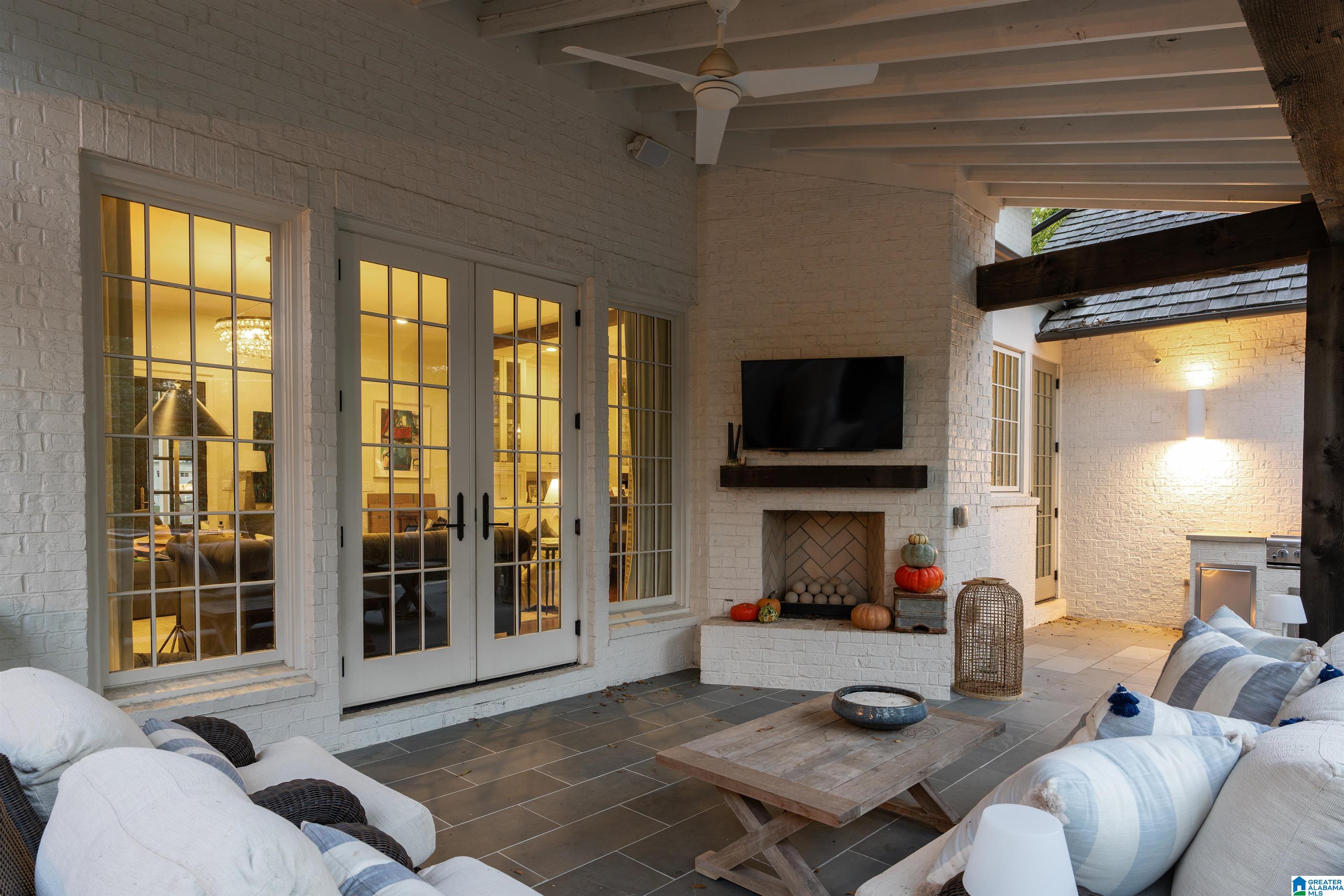 Covered patio with cushioned seating, white brick fireplace, mounted television, and French doors.