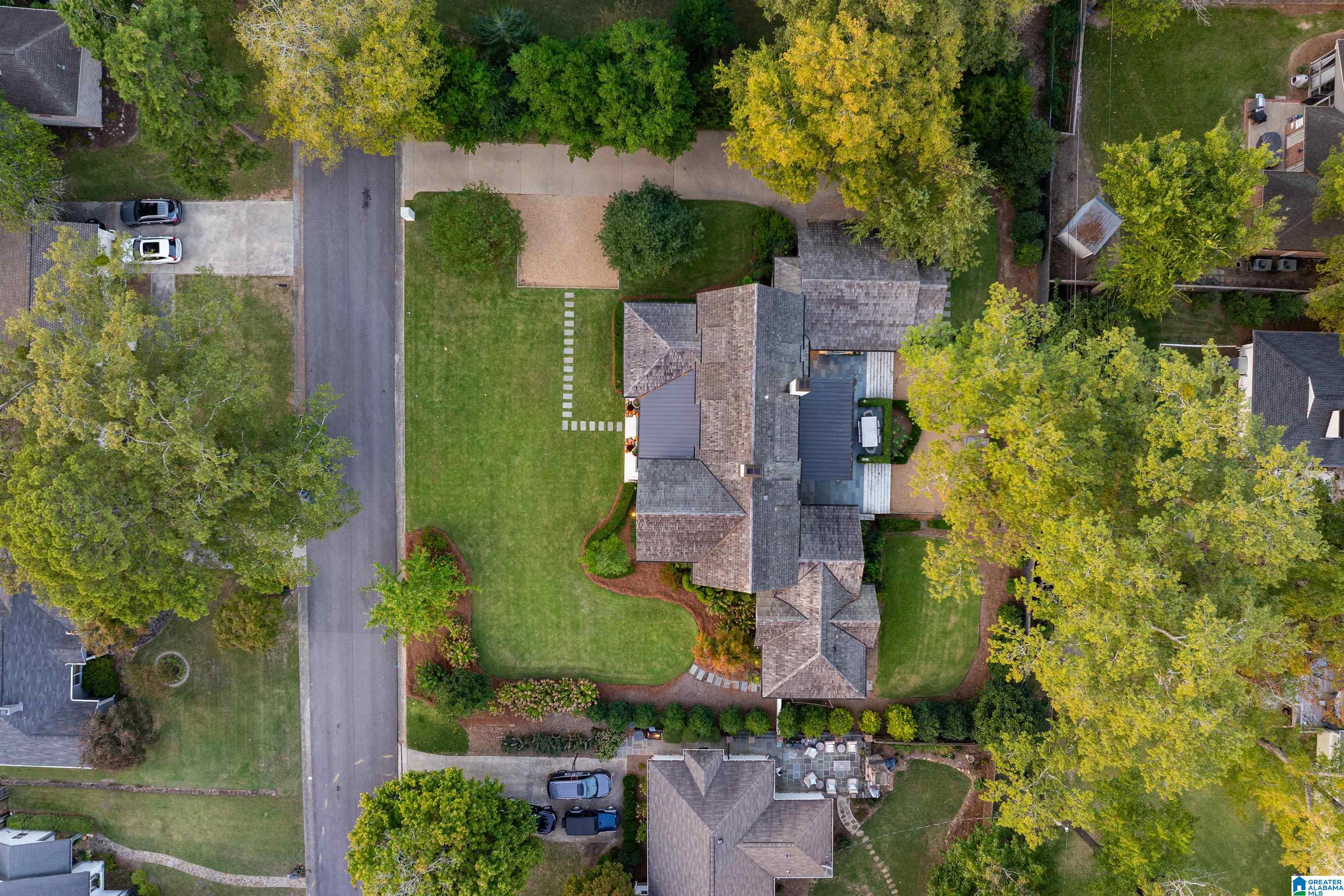 Aerial view of a large home with a broad lawn, landscaped garden beds, and a rear patio.