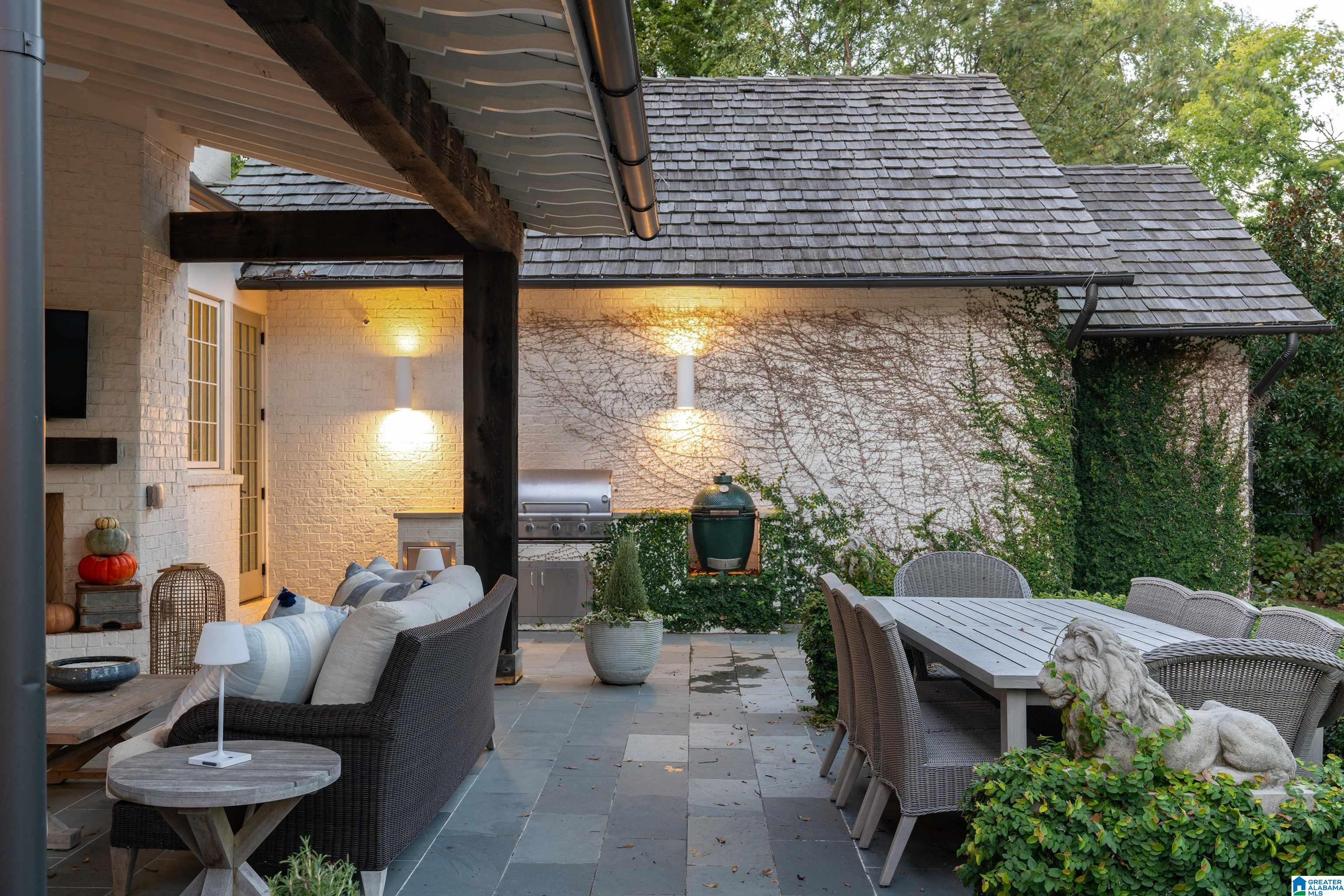 Covered patio with wicker seating, an outdoor kitchen, dining table, and stone lion statue.