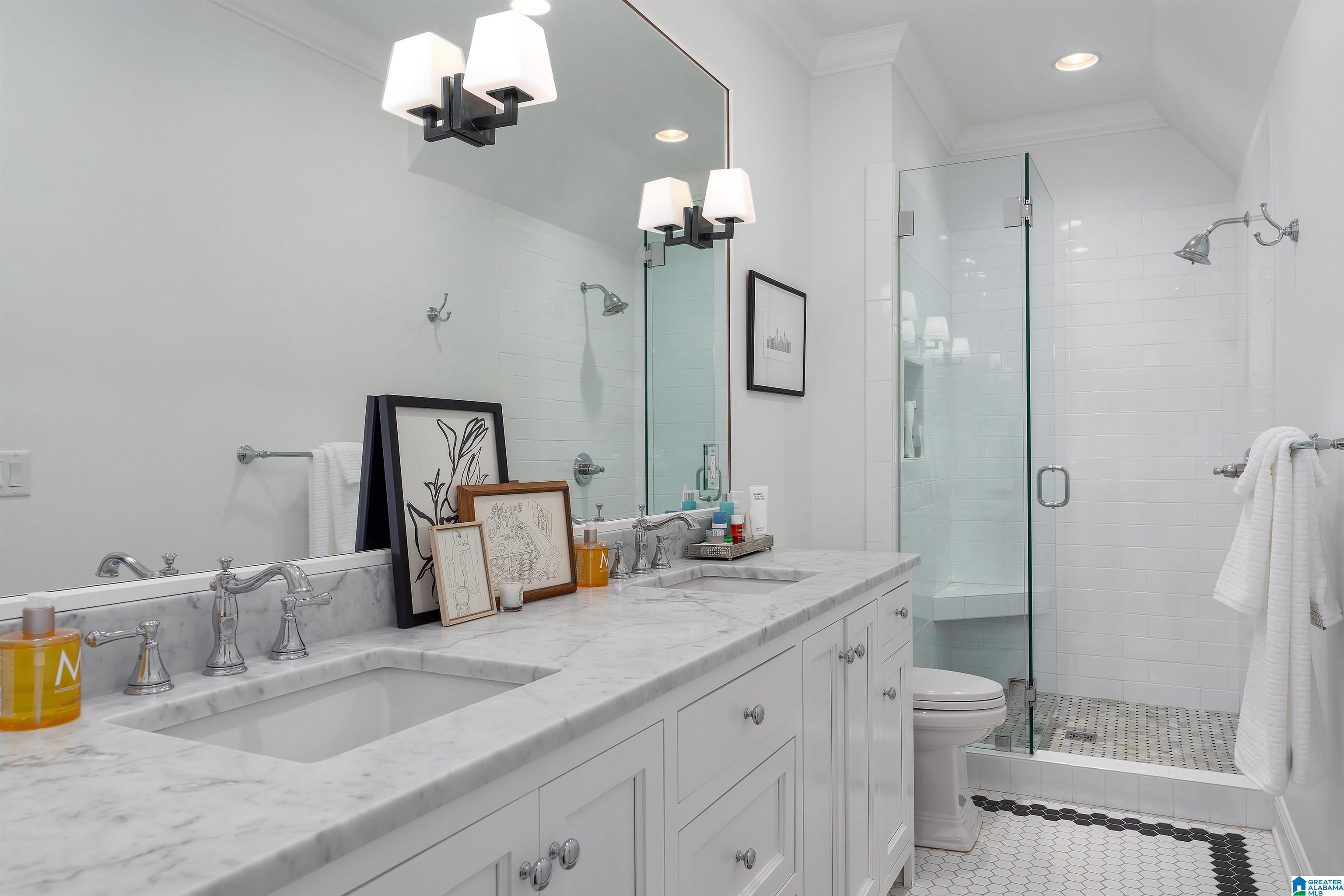 Bright bathroom with a marble double vanity and glass-enclosed tiled shower.