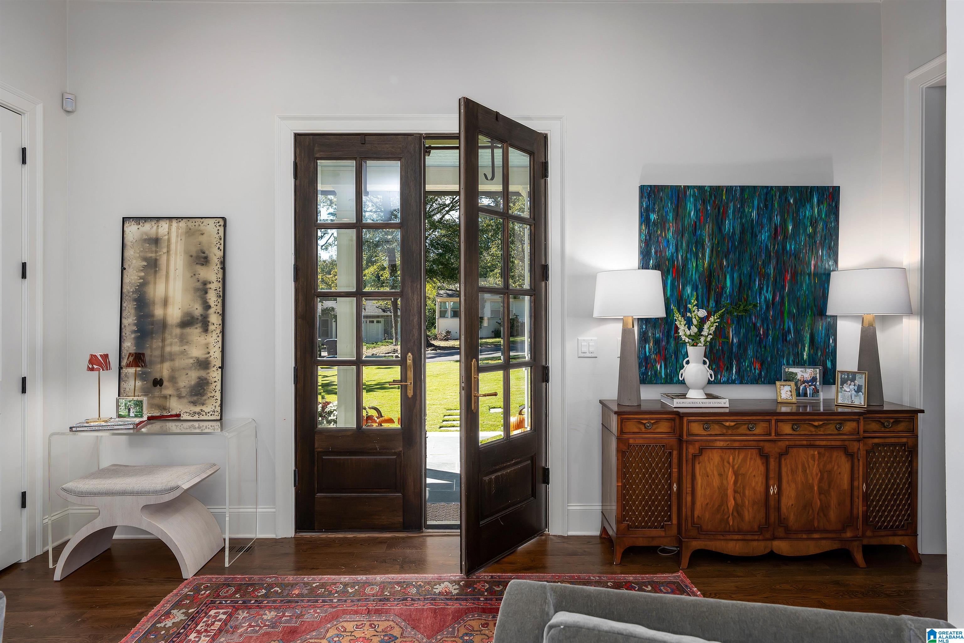 Furnished entry with open glass-paneled doors, a carved sideboard, and colorful abstract art.