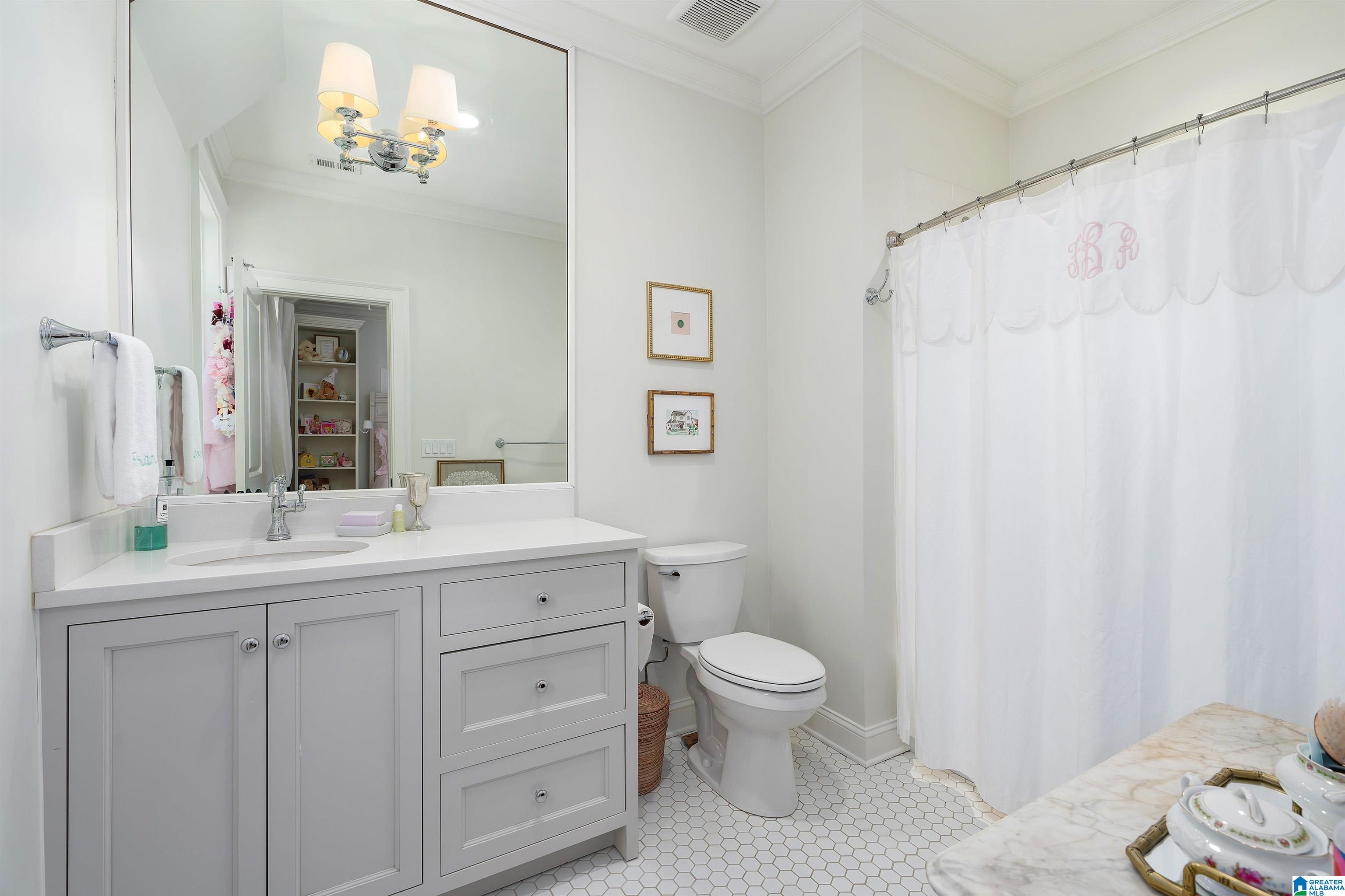 Bathroom with a paneled white vanity, hexagonal tile floor, and monogrammed shower curtain.