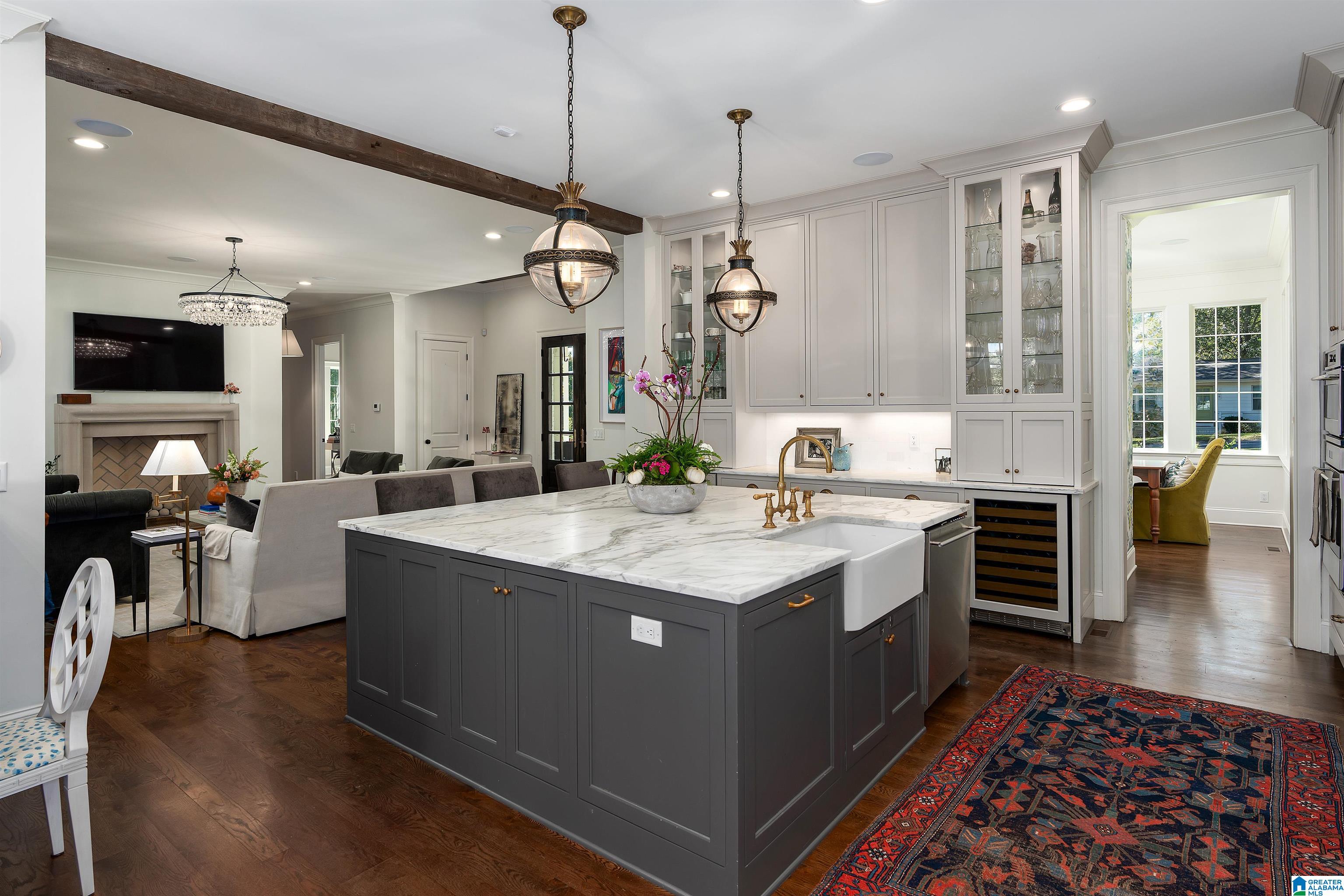Open-plan kitchen with a marble-topped gray island, brass pendants, glass-front cabinets, and adjoining living room.