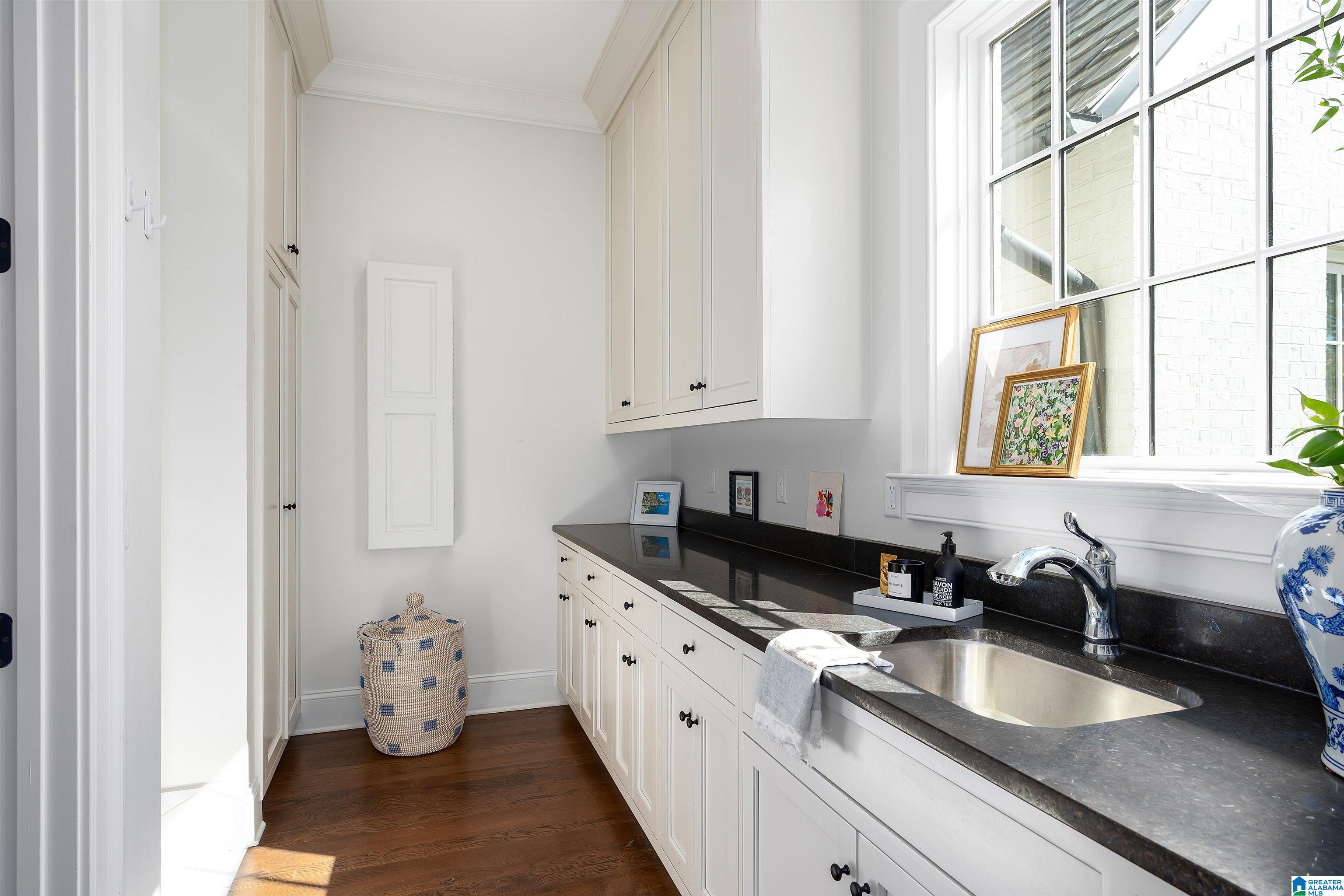Laundry room with white cabinets, dark countertops, and a sink beneath a large window.