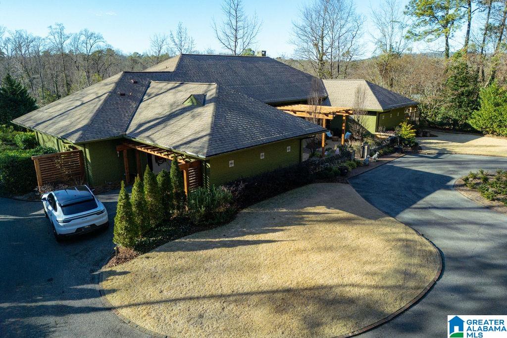 Large green residence with multiple shingle roofs and a curved driveway, viewed from above.