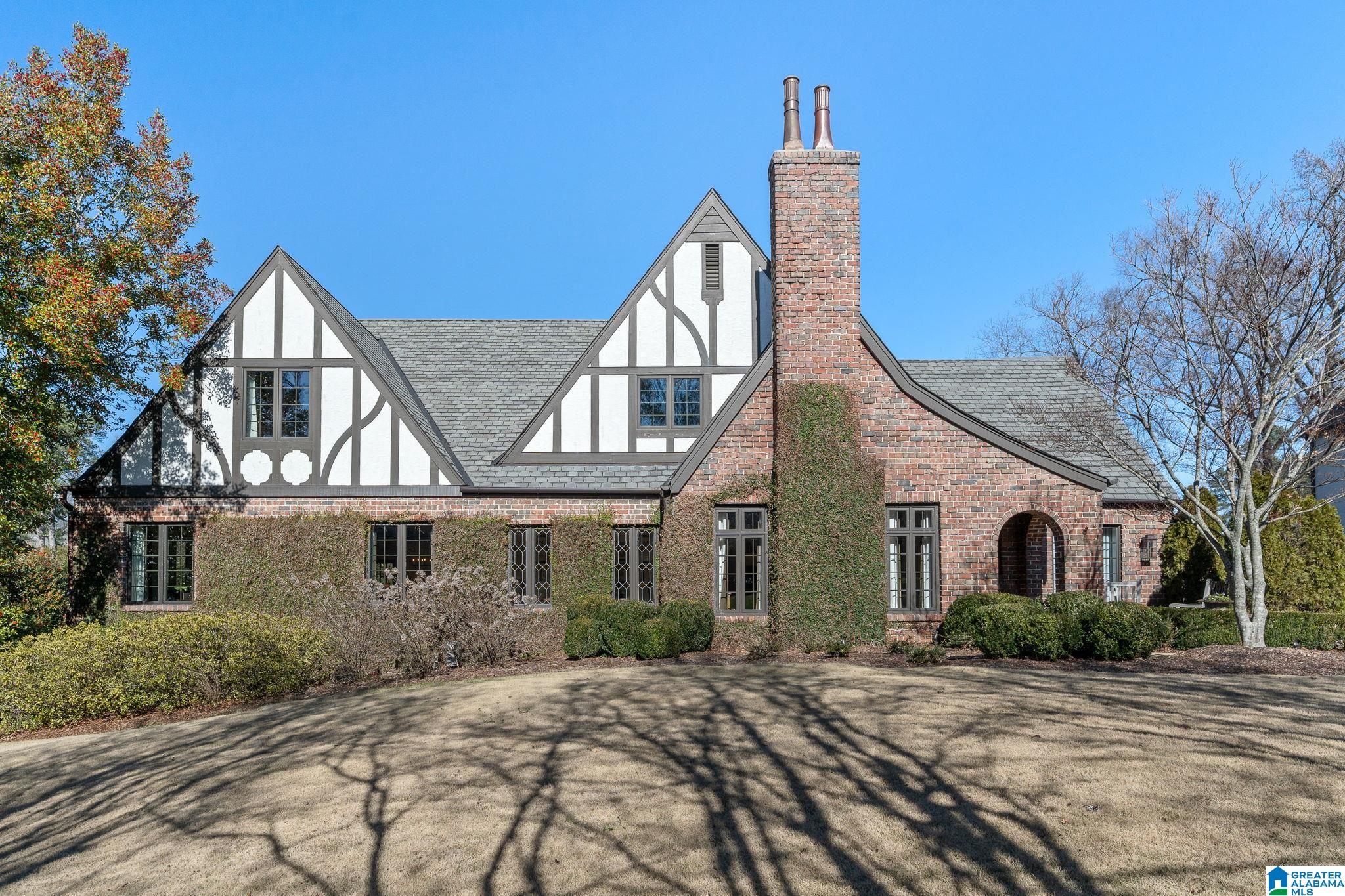 Tudor-style brick house with half-timbered gables, a tall chimney, and a broad front lawn.