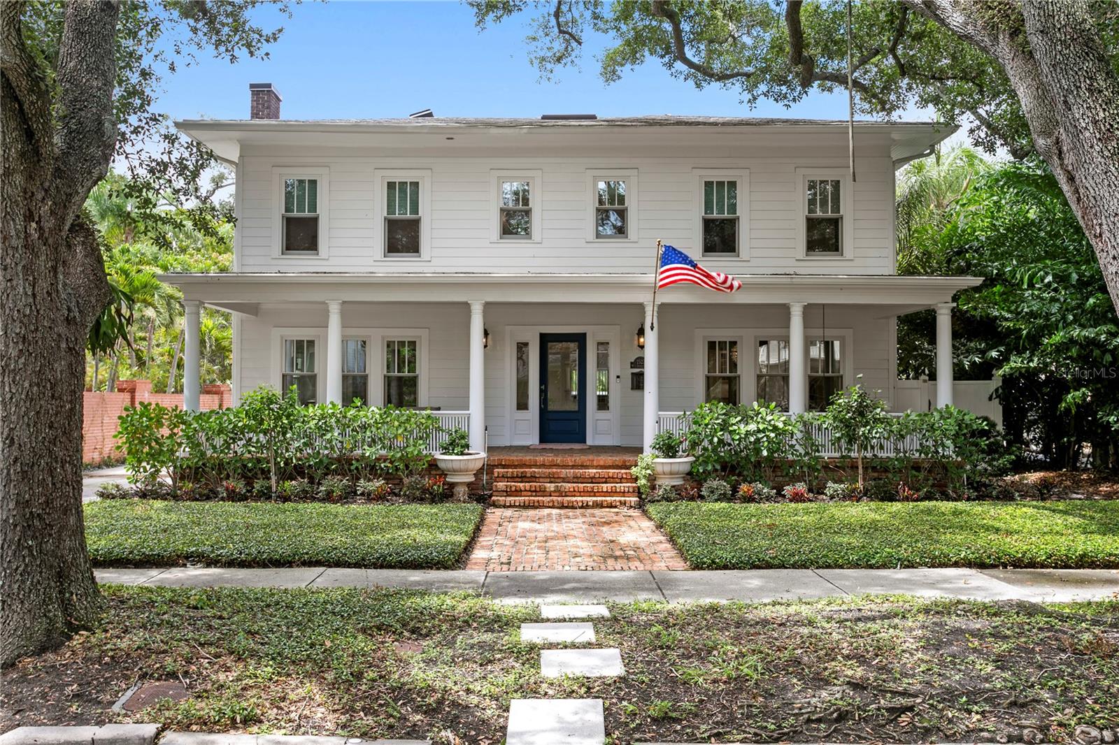 White two-story house with a columned porch, blue front door, and American flag.