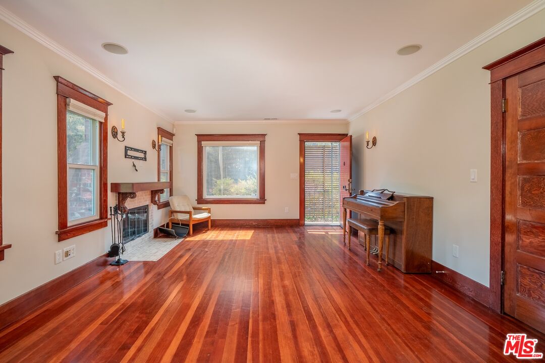 Living room with polished hardwood floors, a fireplace, and a piano beside a glass door.