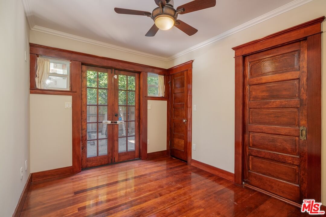 Empty room with polished hardwood floors, rich wood trim, glass-paneled doors, and a ceiling fan.