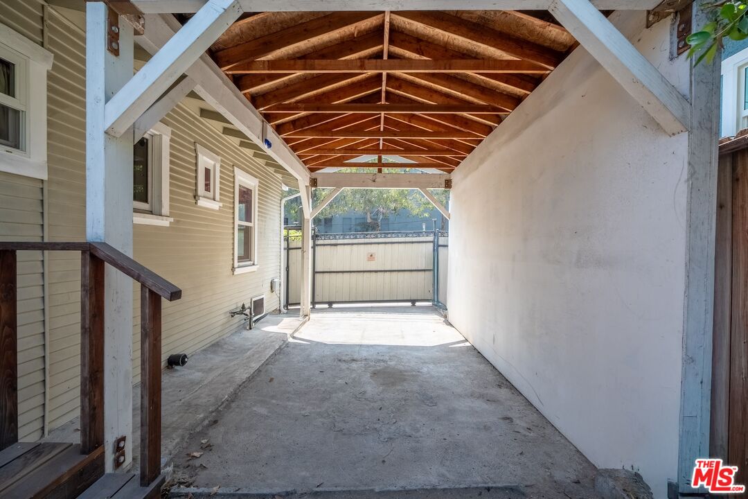 Covered carport with exposed timber roof trusses and a metal gate at the far end.