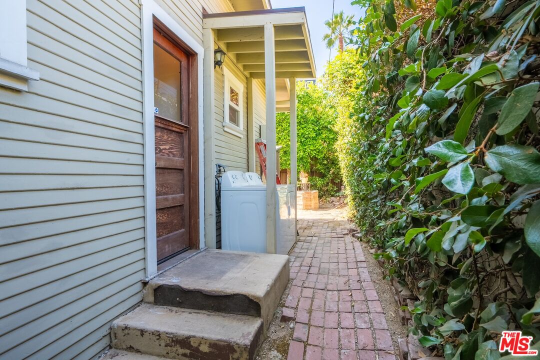 House side entrance with exterior laundry beside a brick walkway and dense greenery.