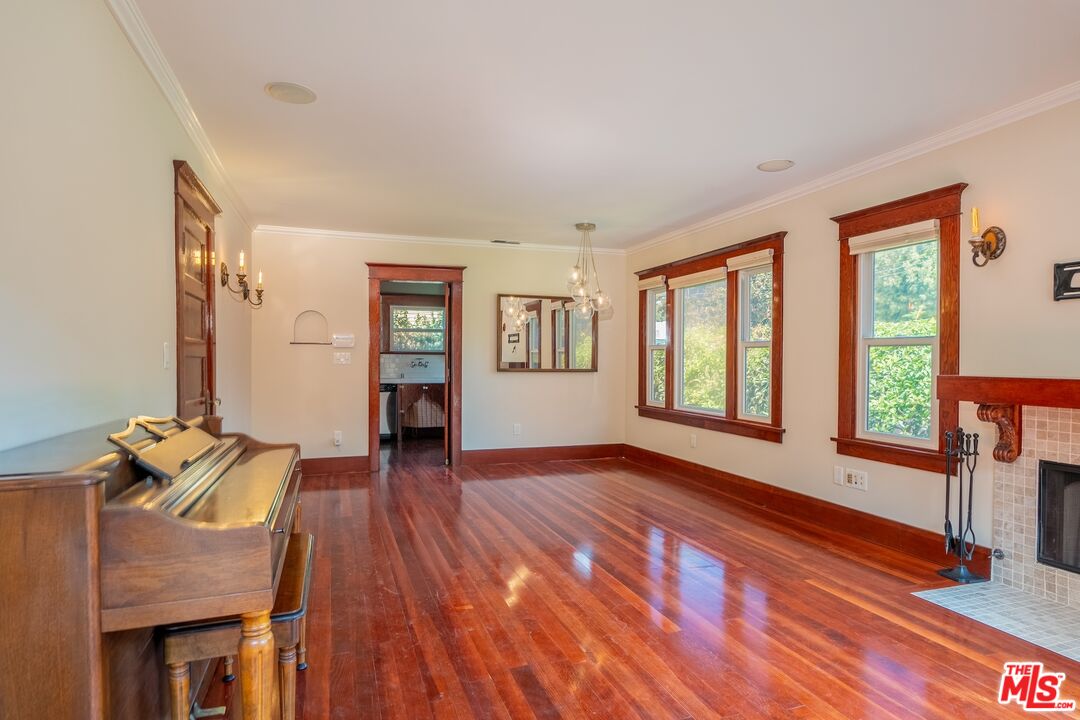 Living room with a piano, tiled fireplace, and tall wood-trimmed windows.