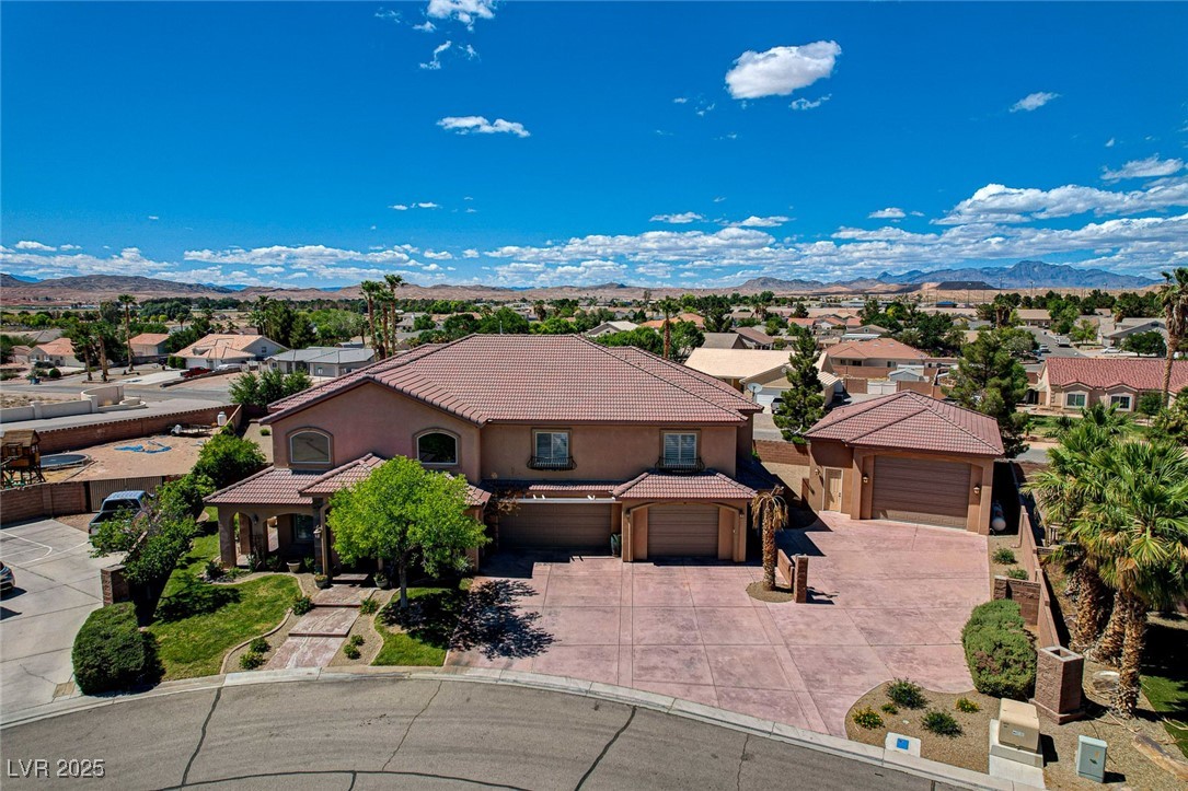 Aerial view of a two-story stucco home with multiple garages, a broad driveway, and distant mountains.