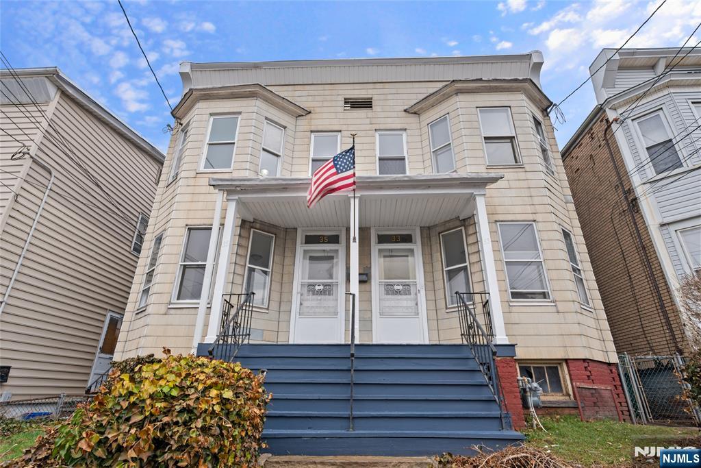 Two-story beige duplex with paired entrances, blue front steps, and an American flag above the porch.