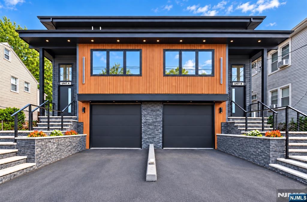 Modern two-unit home with orange wood siding, two dark garage doors, and separate stairway entrances.