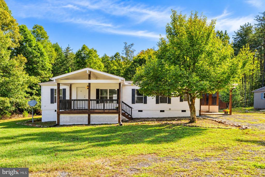 White single-story home with a covered porch, dark railings, and mature trees around the grassy lot.